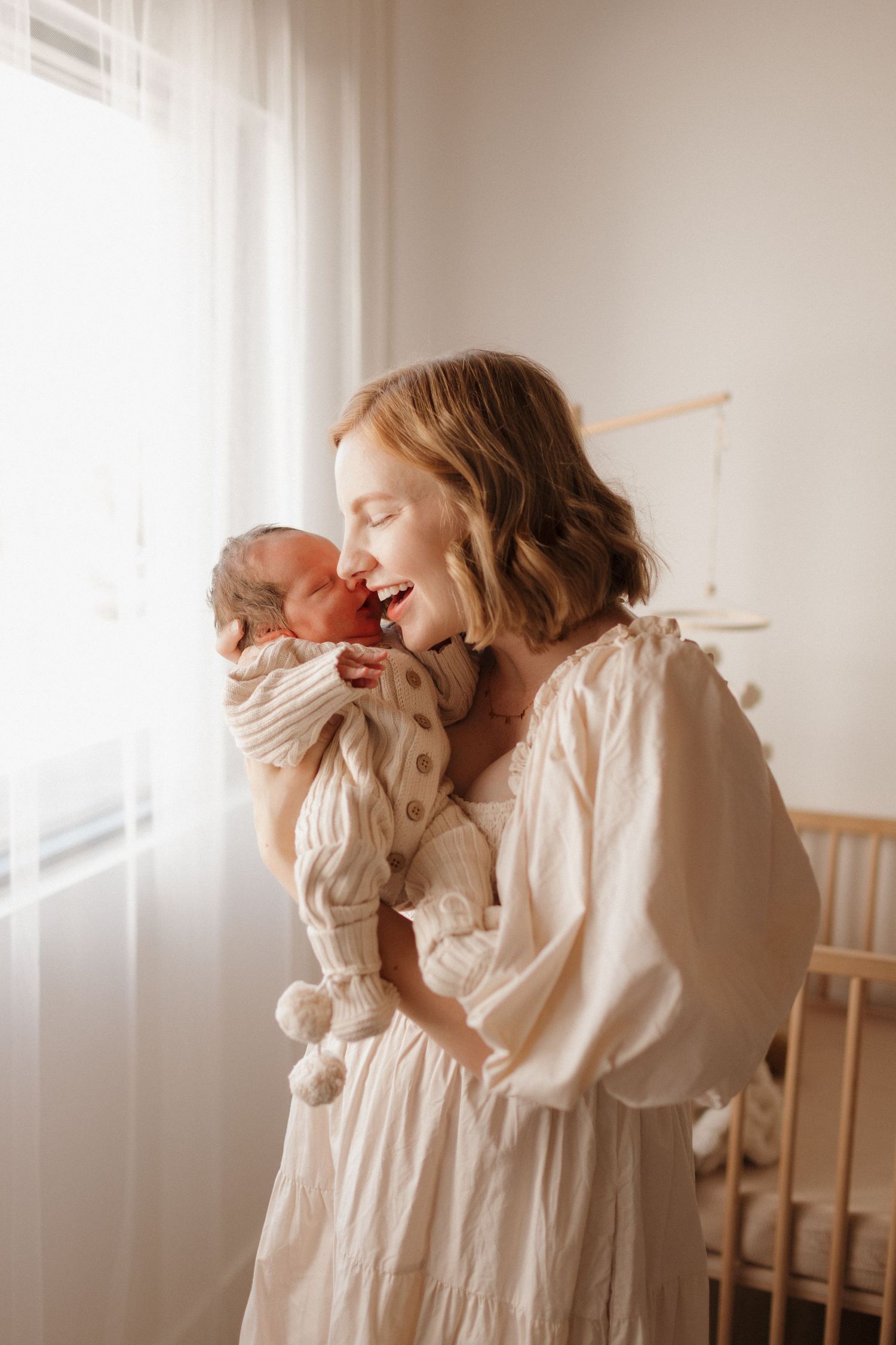 A tender moment between a mother and newborn baby in a sunlit nursery.