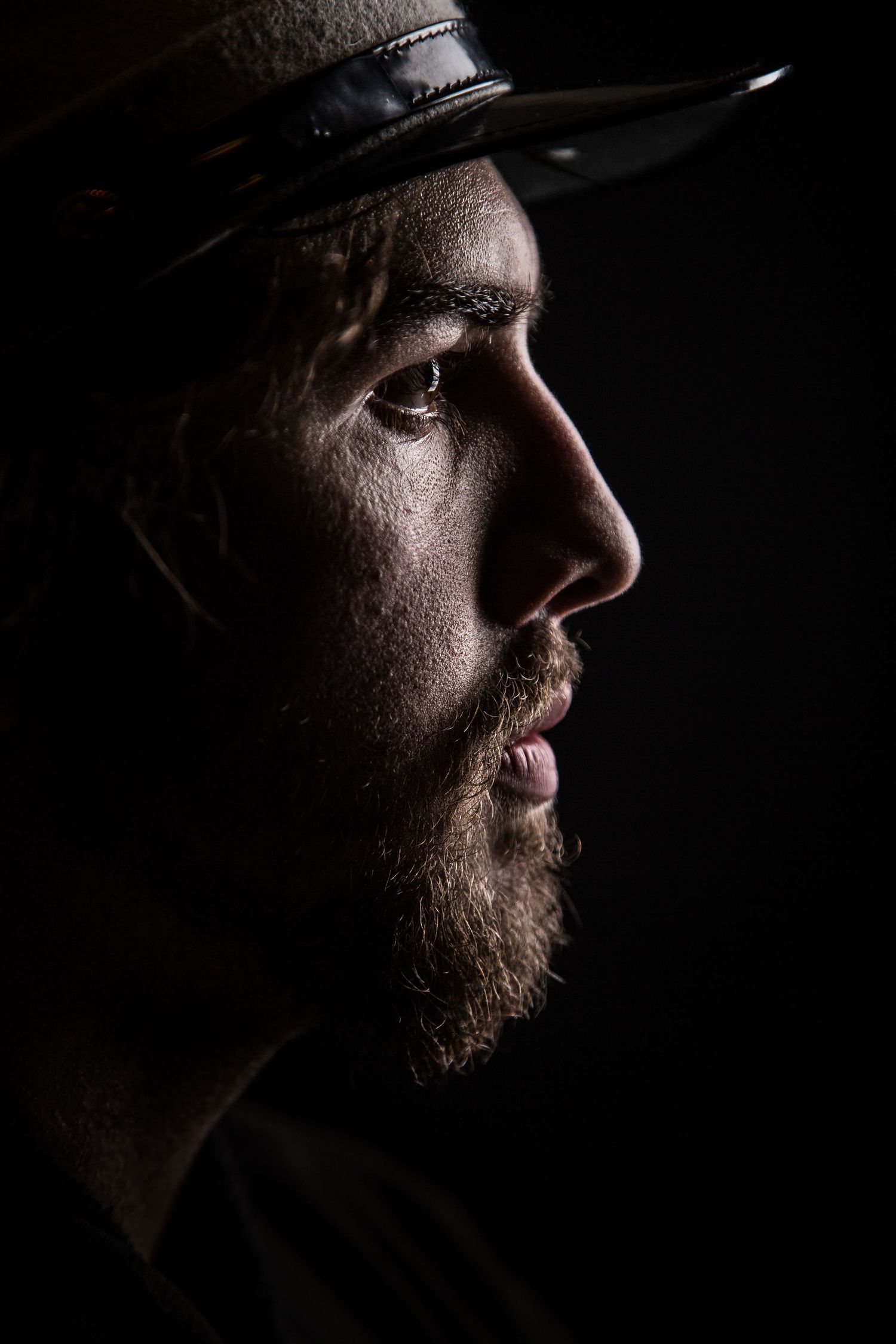 A dramatic side profile portrait shows a person wearing a hat in low-key lighting.