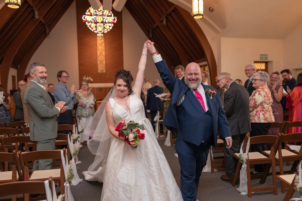 A joyful couple celebrates after their wedding ceremony in a church with wooden pews and a crystal chandelier.