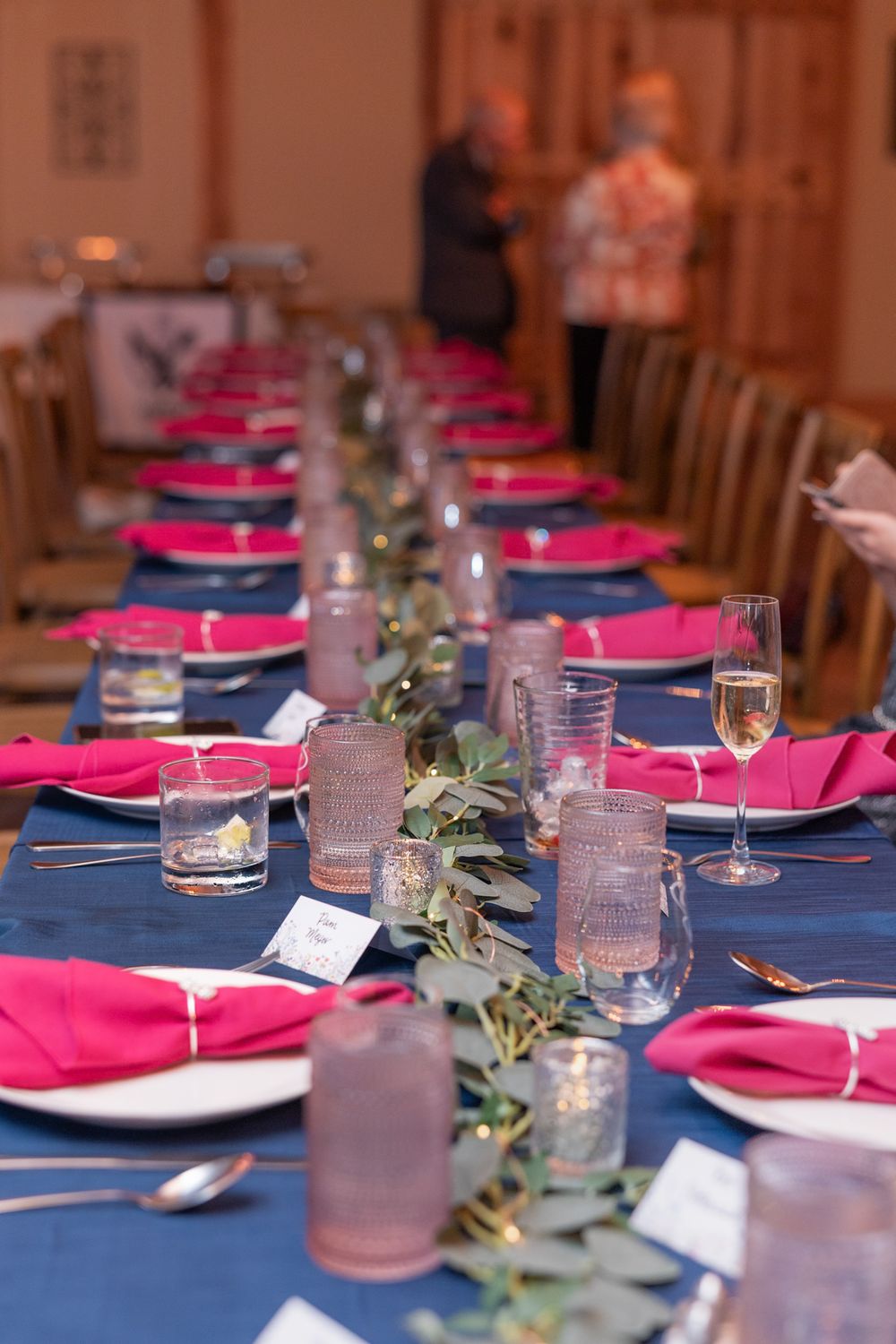 Elegant table setting with navy blue tablecloth and hot pink napkins decorated with greenery for a wedding reception.