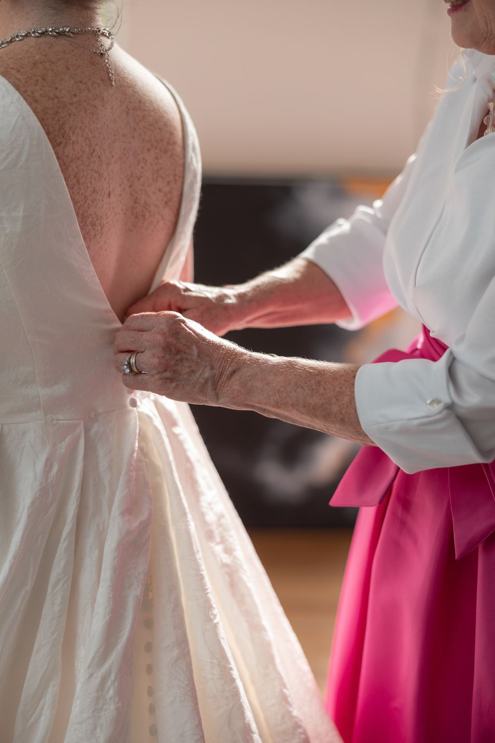 Wedding guests in white dresses and bright pink skirts stand together in an elegant group formation.