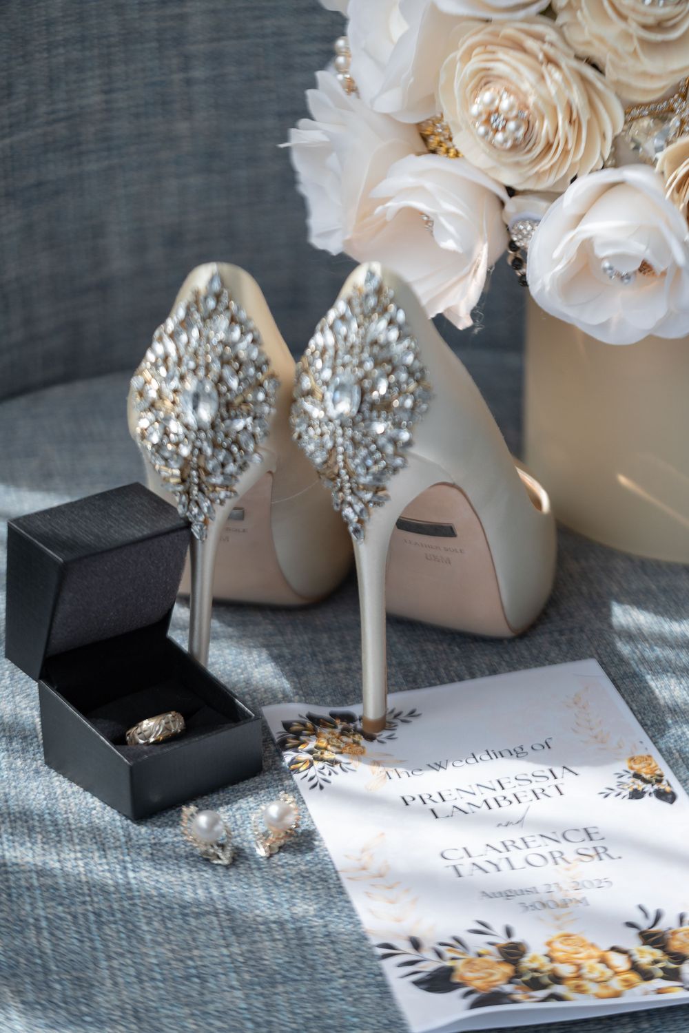 Elegant white bridal shoes with crystal embellishments displayed alongside white roses and wedding invitations.