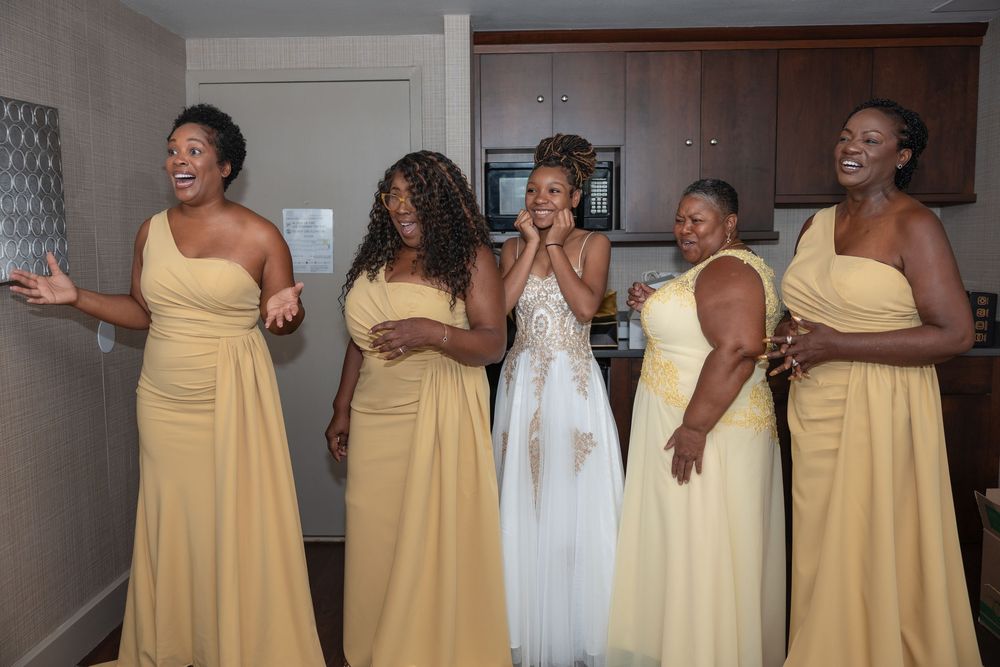 Bridesmaids in matching yellow dresses pose and laugh together during a wedding celebration.