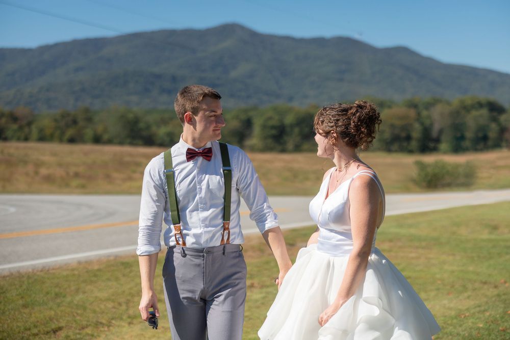 A couple walks hand in hand through a scenic mountain meadow on their wedding day with rolling hills in the background.