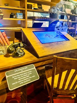 A vintage wood desk with a blue touchscreen display and retro black rotary telephone in a restaurant or office setting.