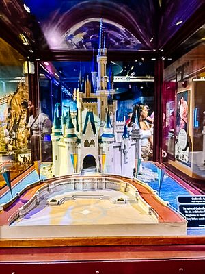 Display model of Cinderella Castle in a museum exhibit case with blue lighting and golden decorative elements.