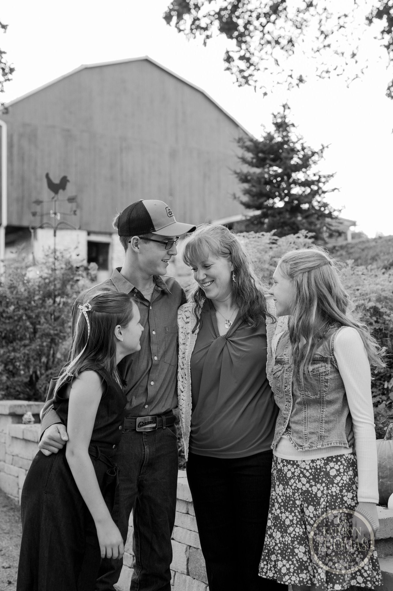 Black and white family portrait taken outside a barn with natural, candid expressions.