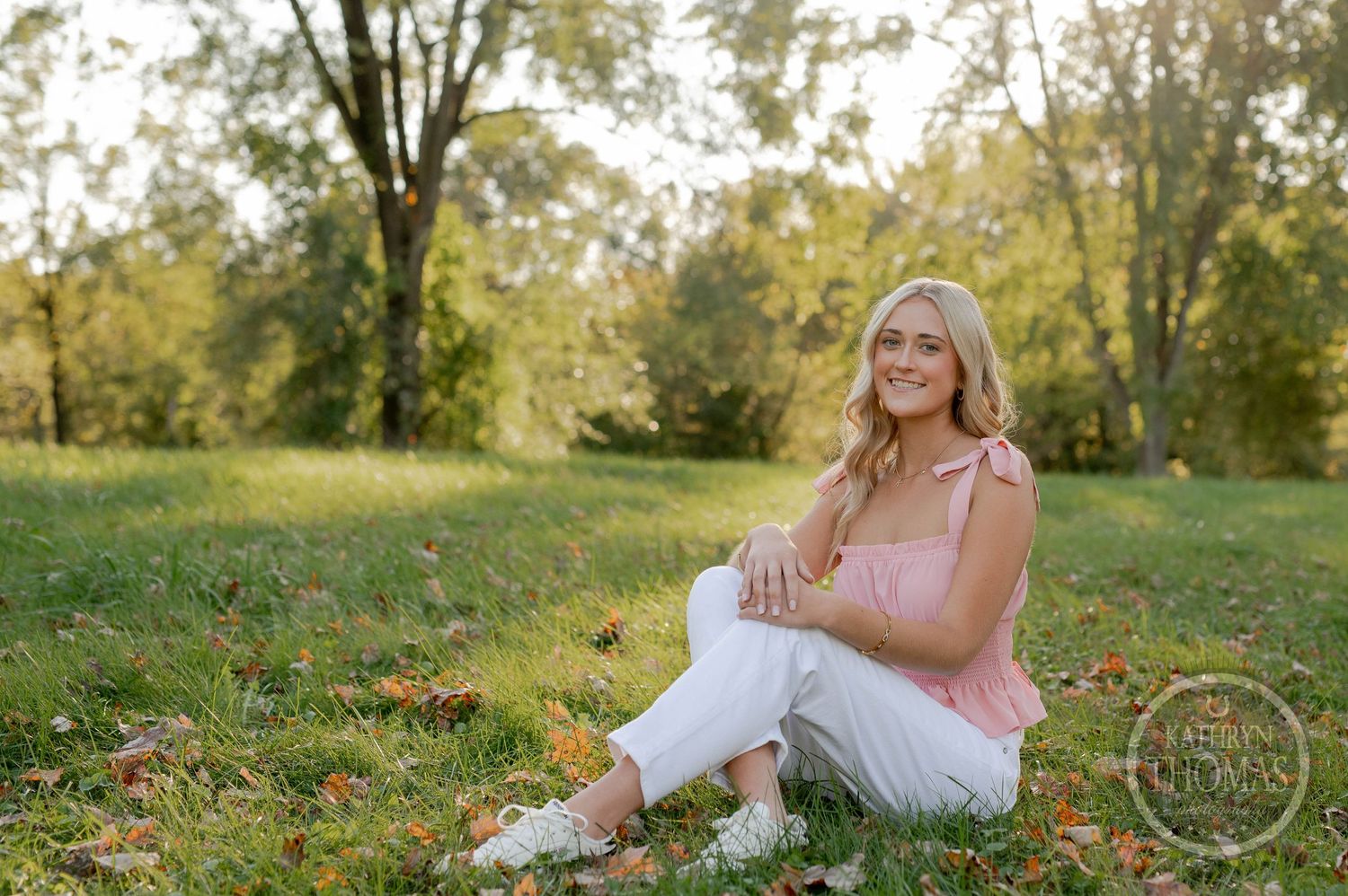 A relaxed outdoor portrait session on grass with trees and autumn leaves in the background.