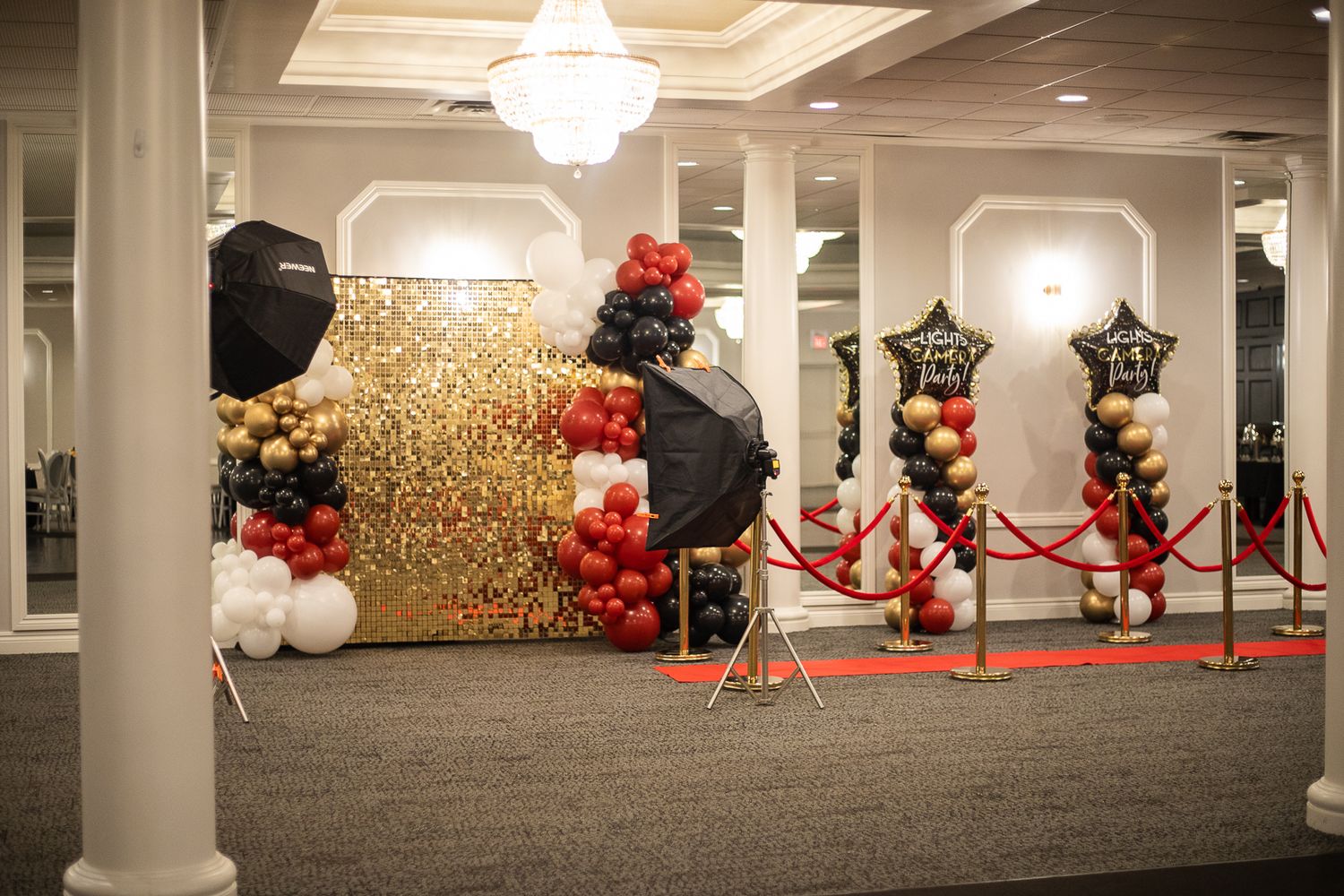 Luxurious ballroom decorated with red carpet, chandeliers, and balloon arrangements.
