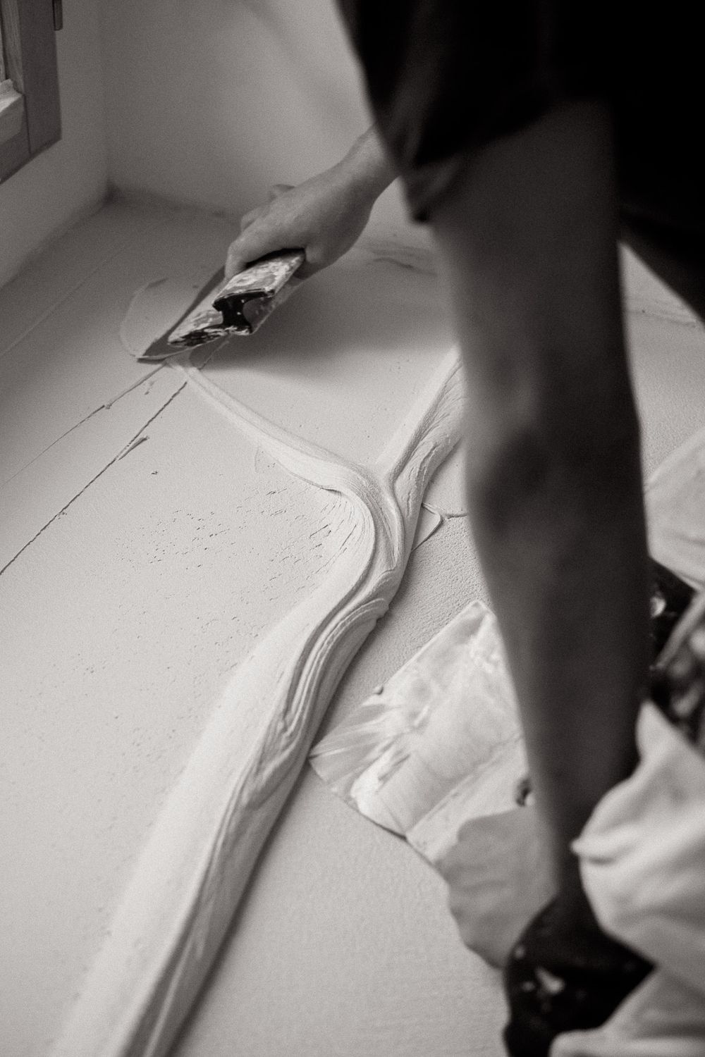 Hand using a trowel to spread white plaster or joint compound on a surface.