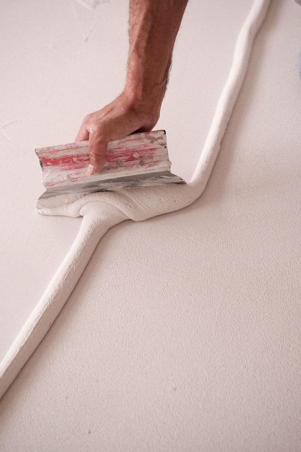 Hand using a metal trowel to smooth white plaster along a wall surface.