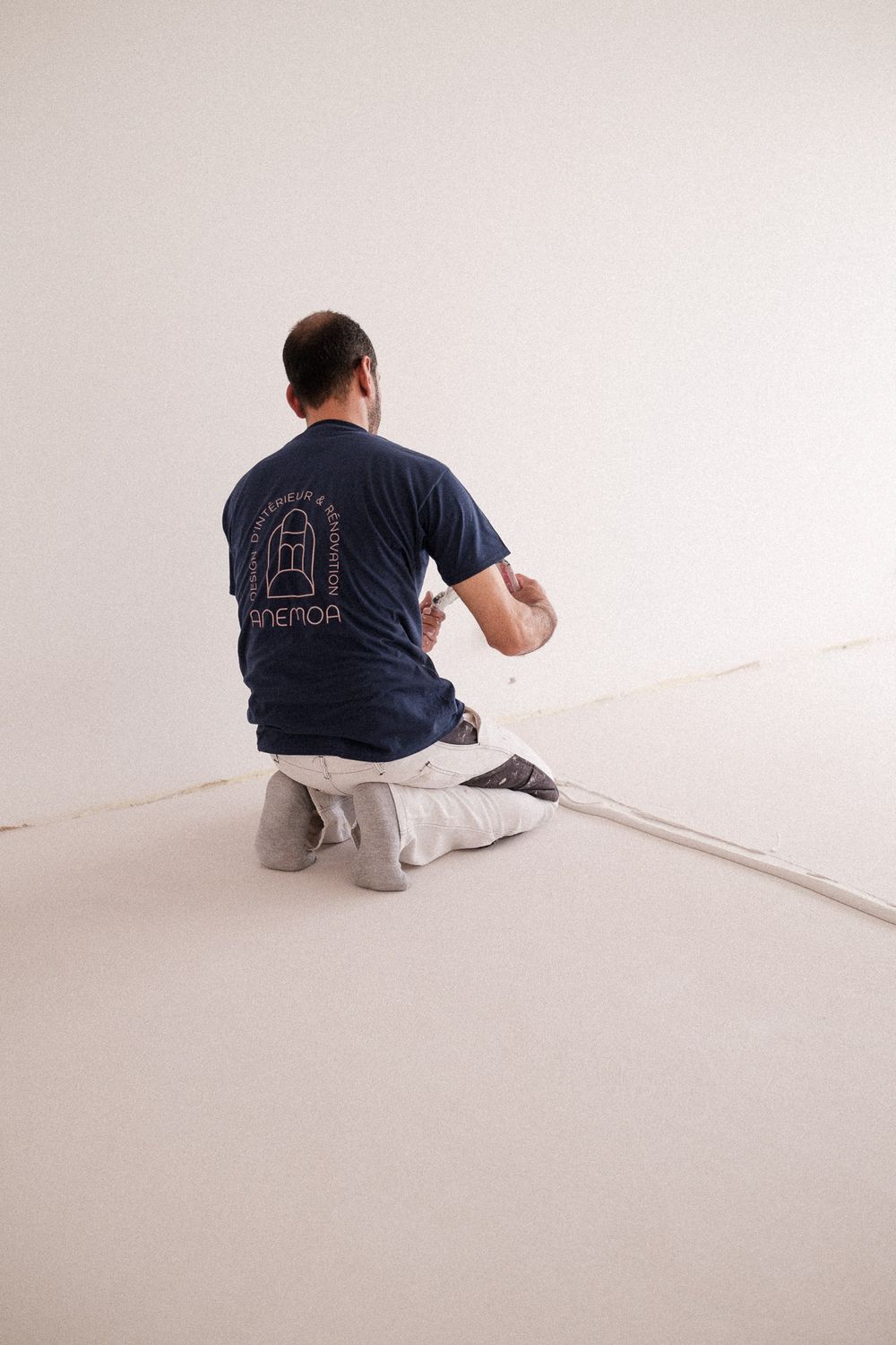 Construction worker in navy t-shirt applying plaster to interior wall while kneeling.