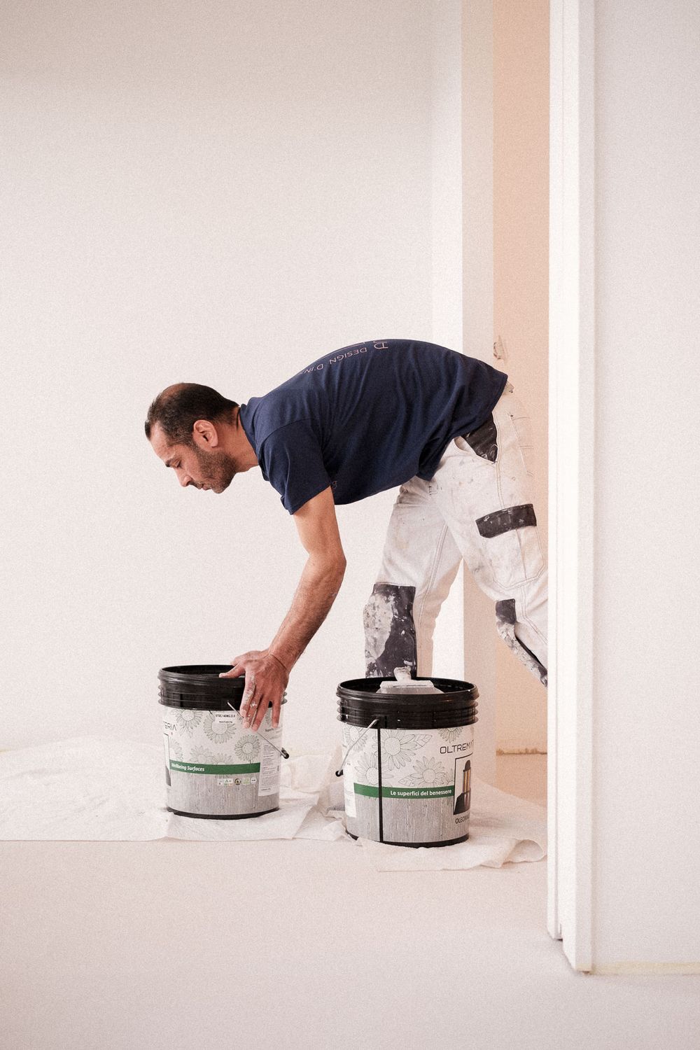 Painter in navy shirt bending over paint buckets during home renovation.