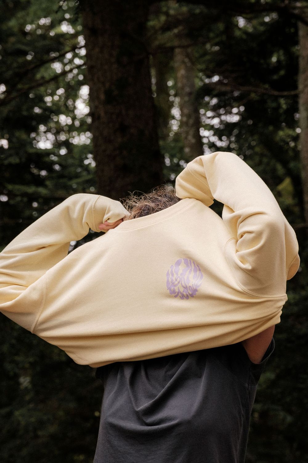 Close-up of a cream colored sweatshirt with embroidered design worn in a wooded setting.