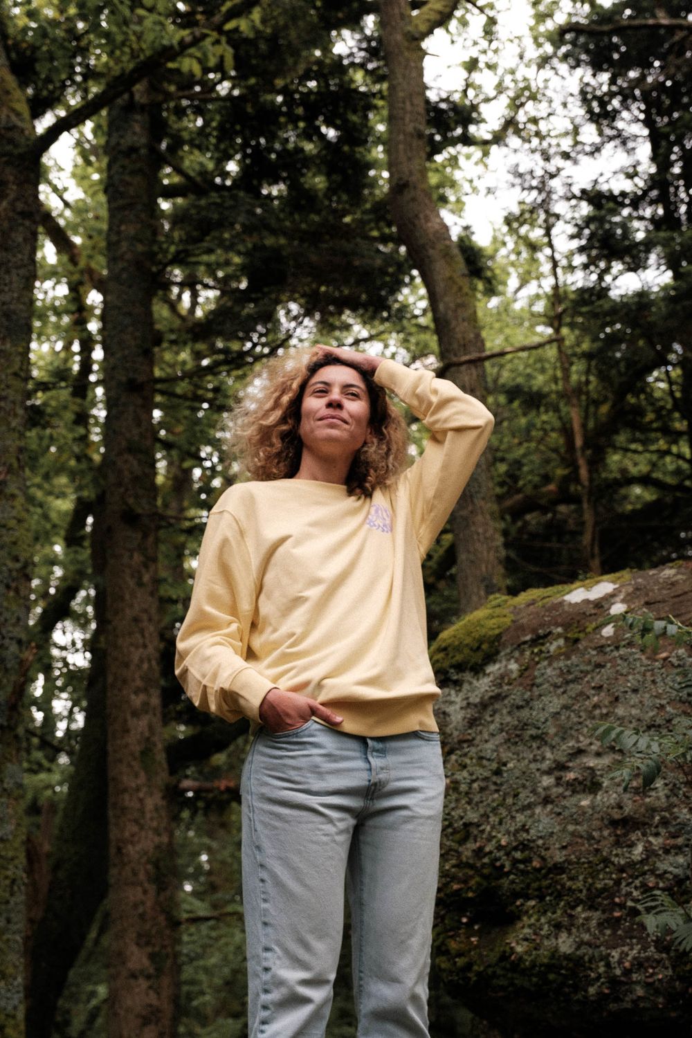 Person in yellow sweater standing against forest backdrop.