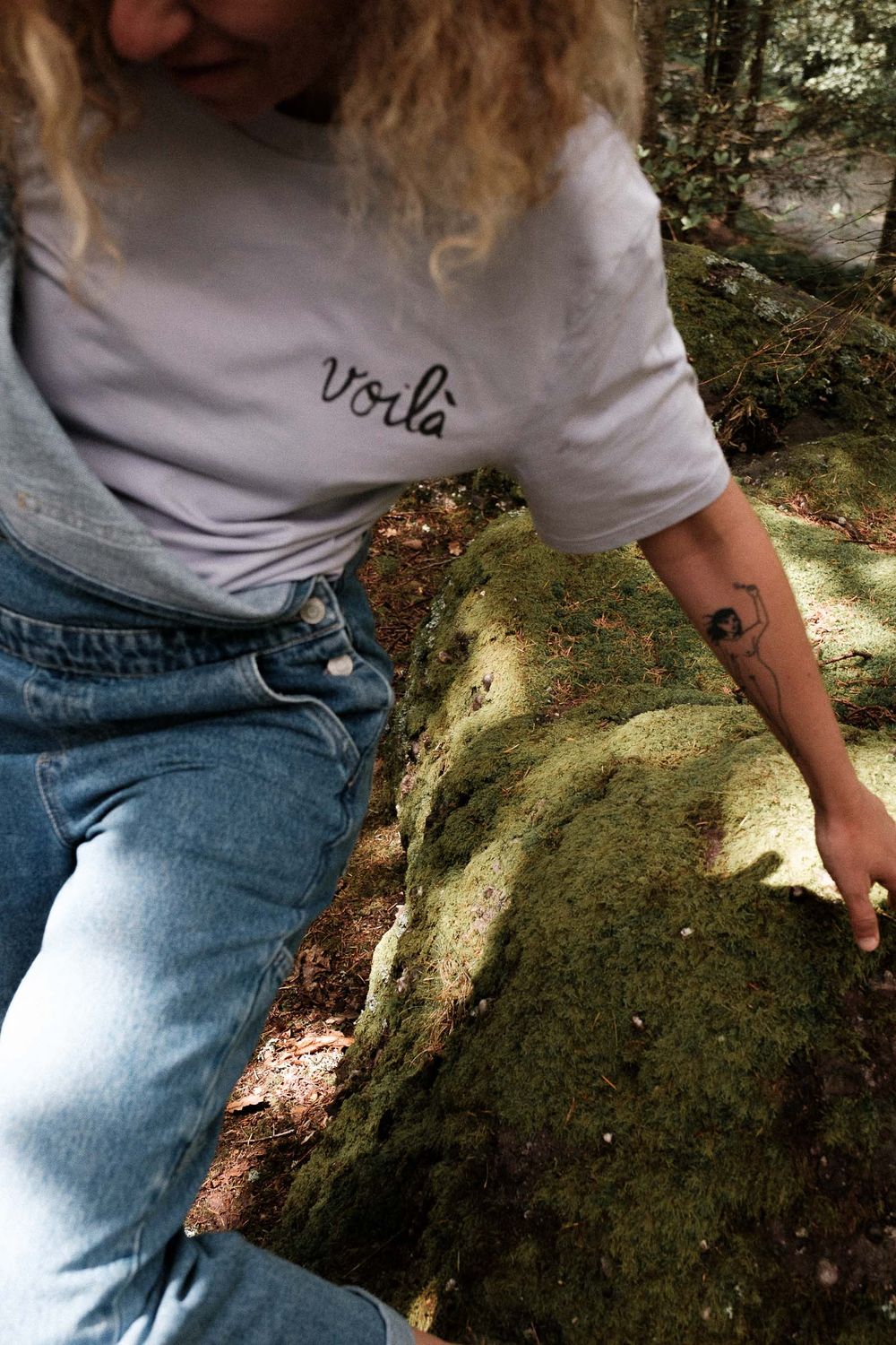 Close-up detail of denim overalls and white t-shirt against mossy rocks in nature.