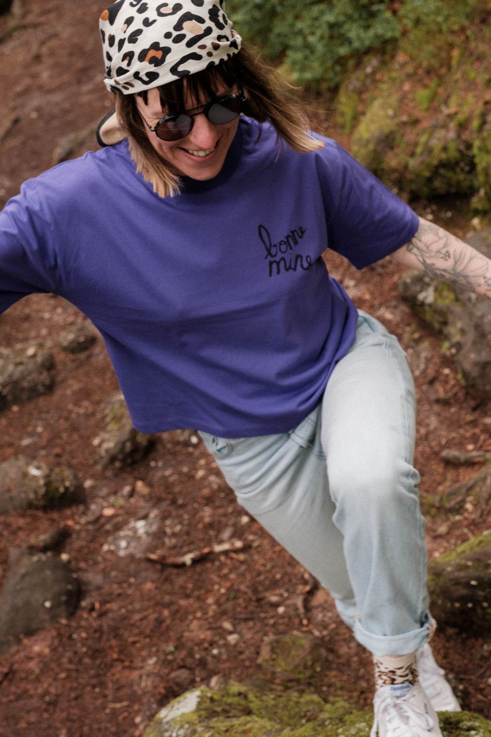 Active hiker in purple sweatshirt and animal print headwear climbing rocky terrain.