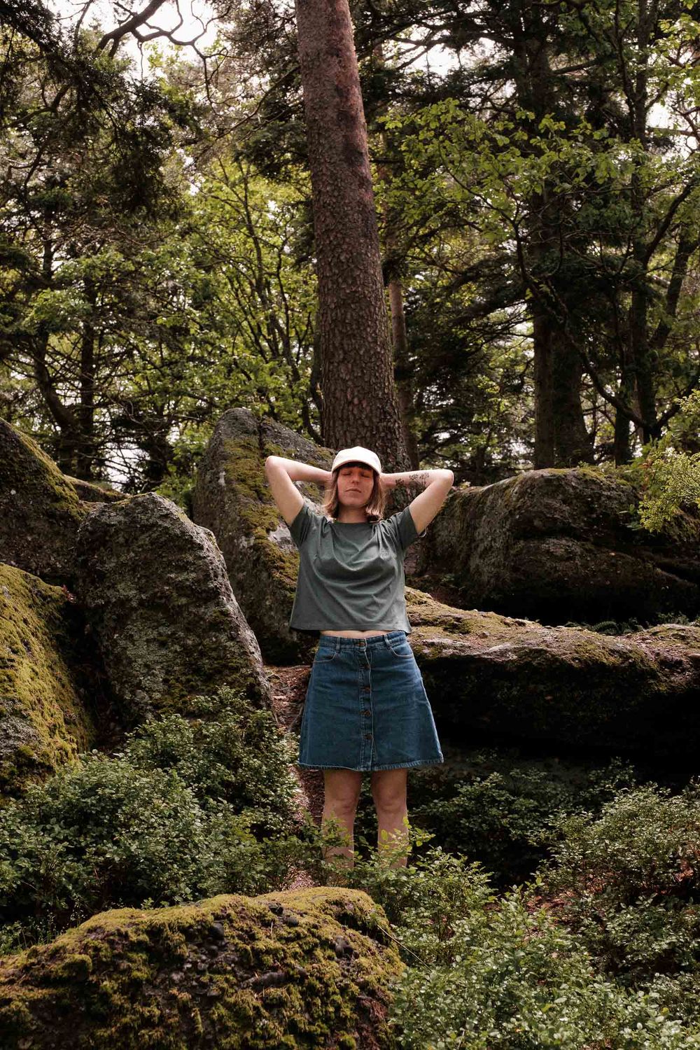 A silhouetted figure stands among mossy rocks in a lush forest setting.