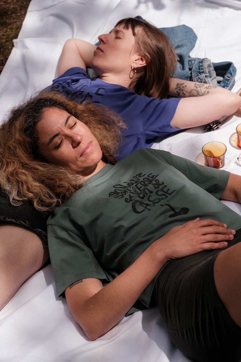 Two people relaxing on white blanket during outdoor picnic wearing casual clothing.