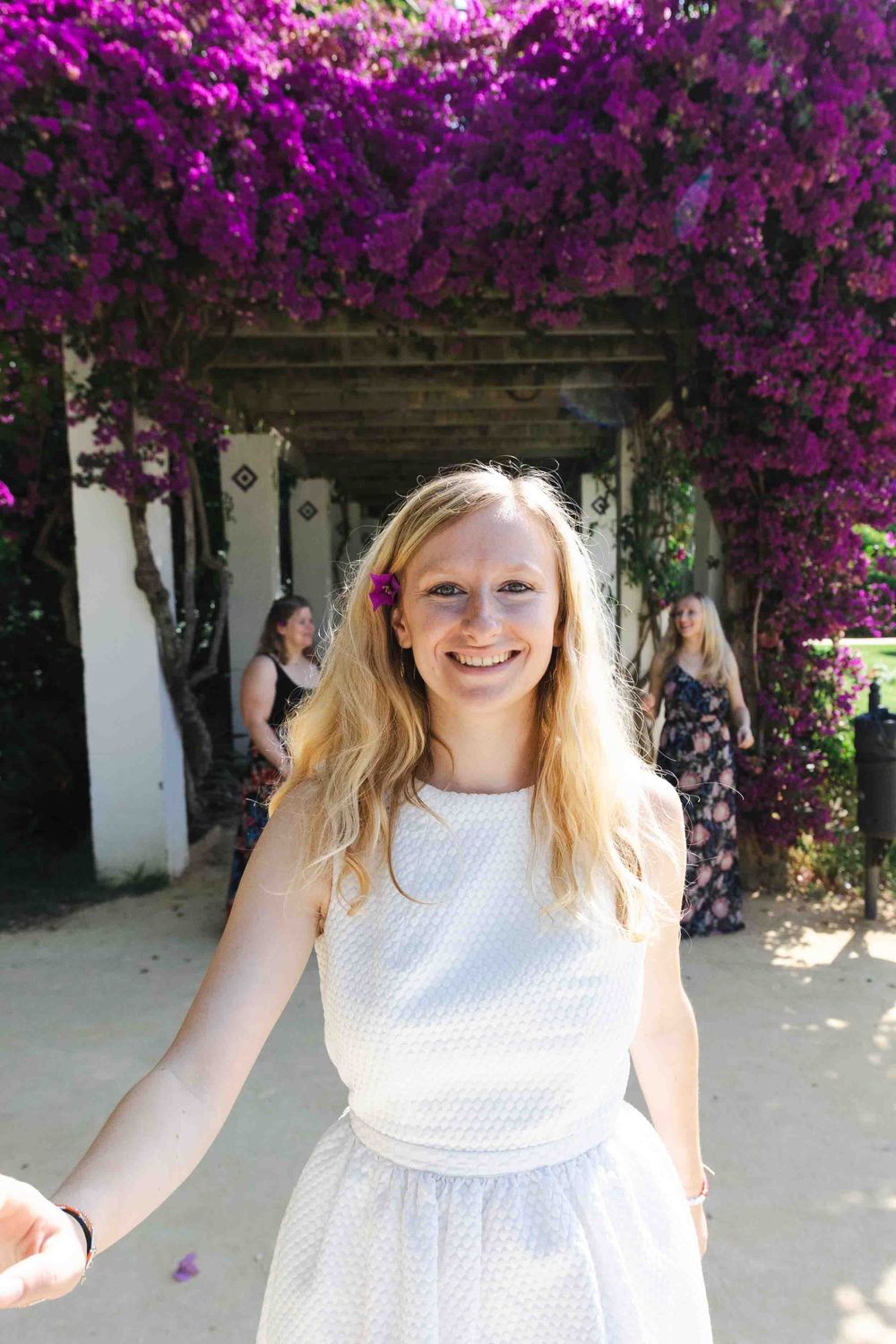 Portraits de groupe EVJF à Séville - Ludiv
A person in a white dress stands beneath a stunning arch of vibrant purple bougainvillea flowers.