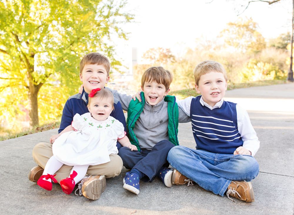Four children sitting together outdoors on a sidewalk during a sunny fall day.