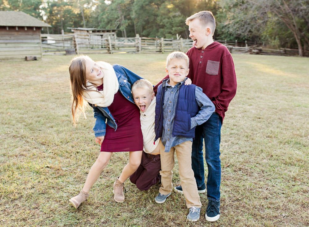 Four siblings playing and being silly together in a rustic outdoor setting.