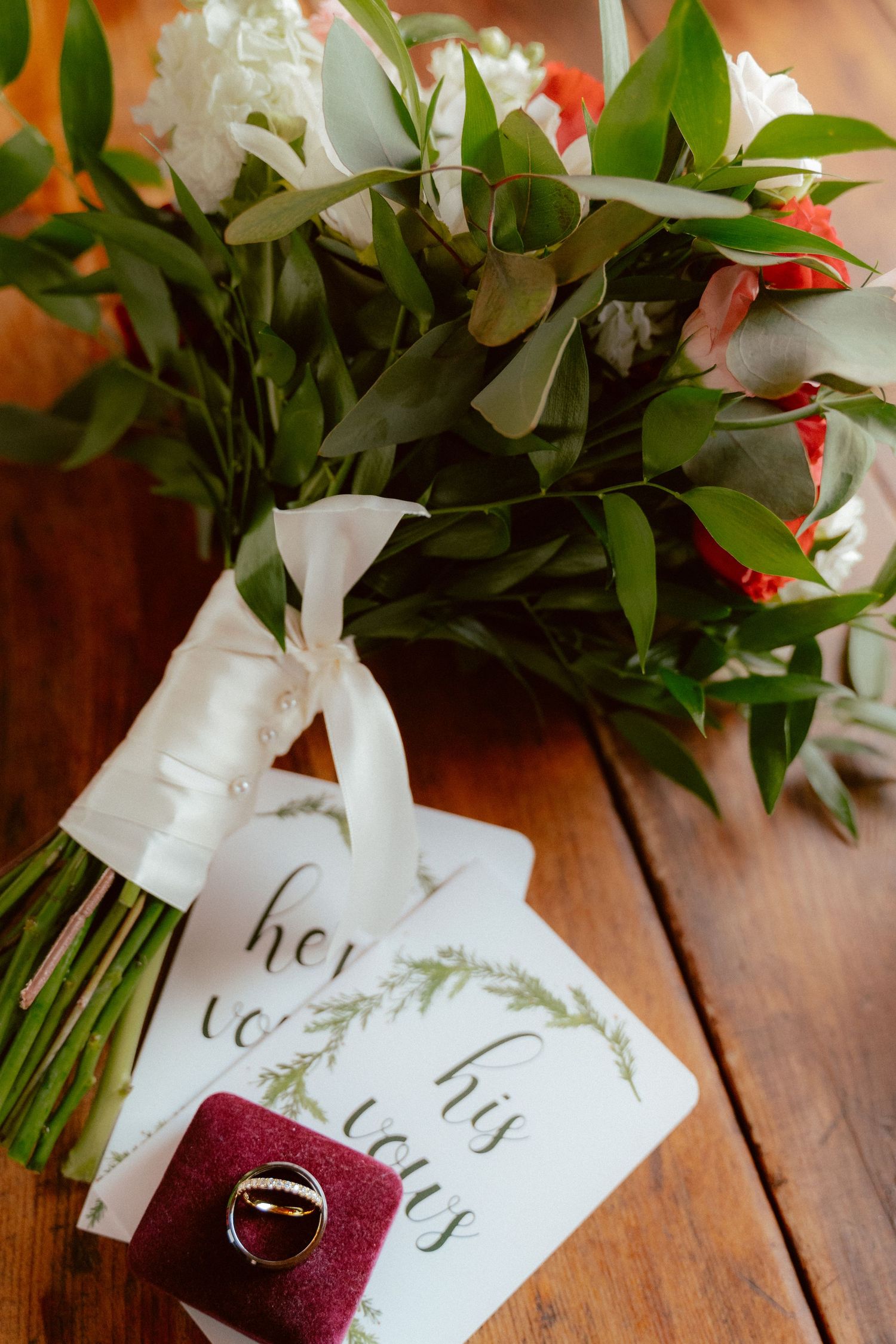 Wedding bouquet with white flowers and handwritten tags tied with ribbon on wooden surface.