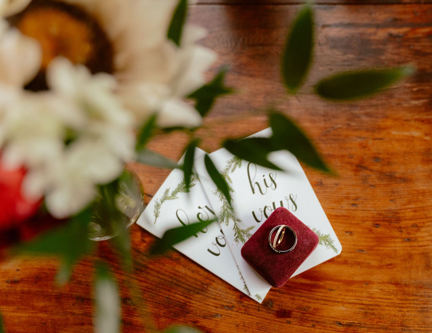 Wedding vow cards and wax seal lying on a rustic wooden table with soft white floral bouquet in background.