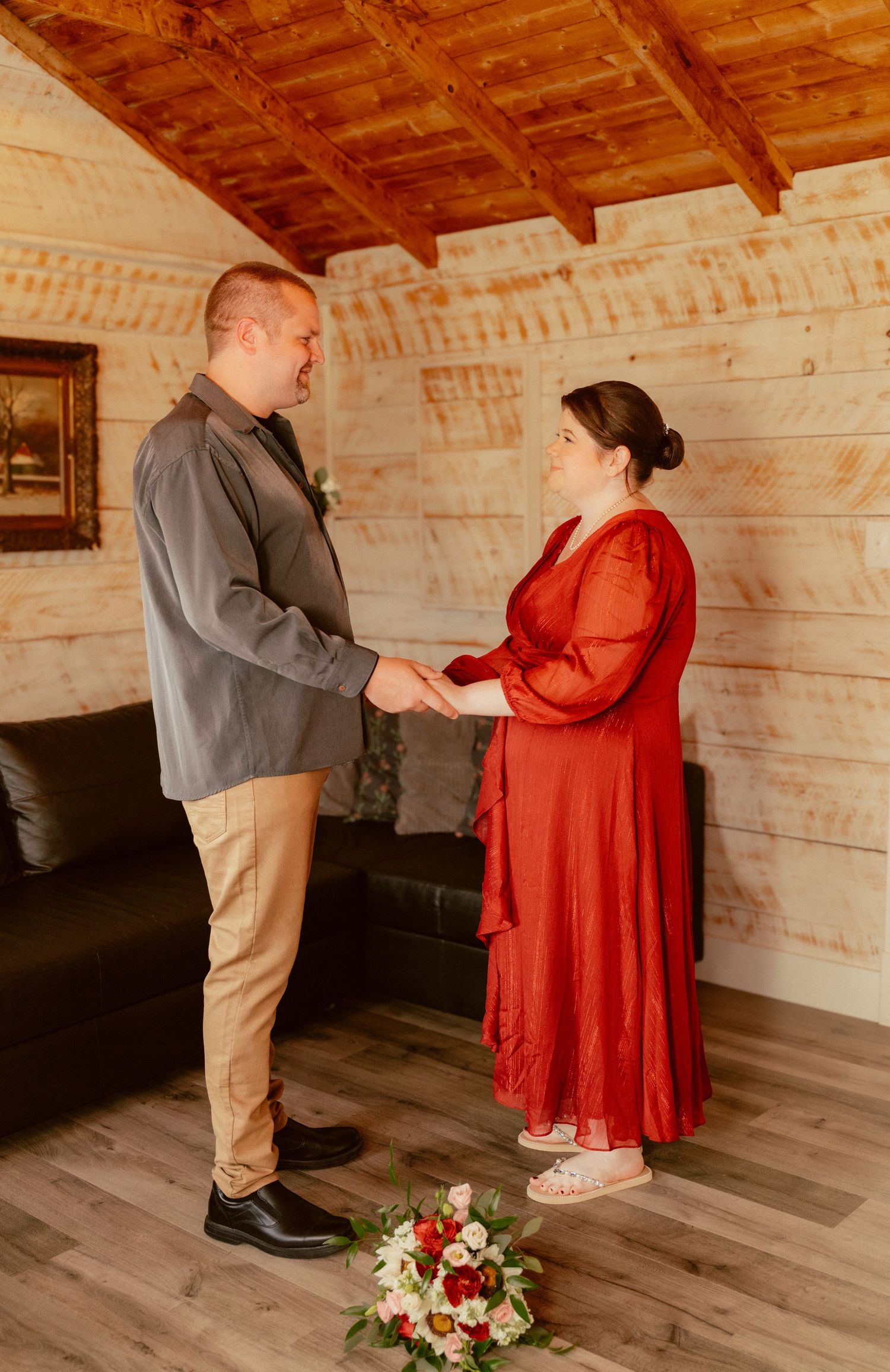 A couple shares an intimate moment in a rustic wooden cabin with a floral bouquet at their feet.