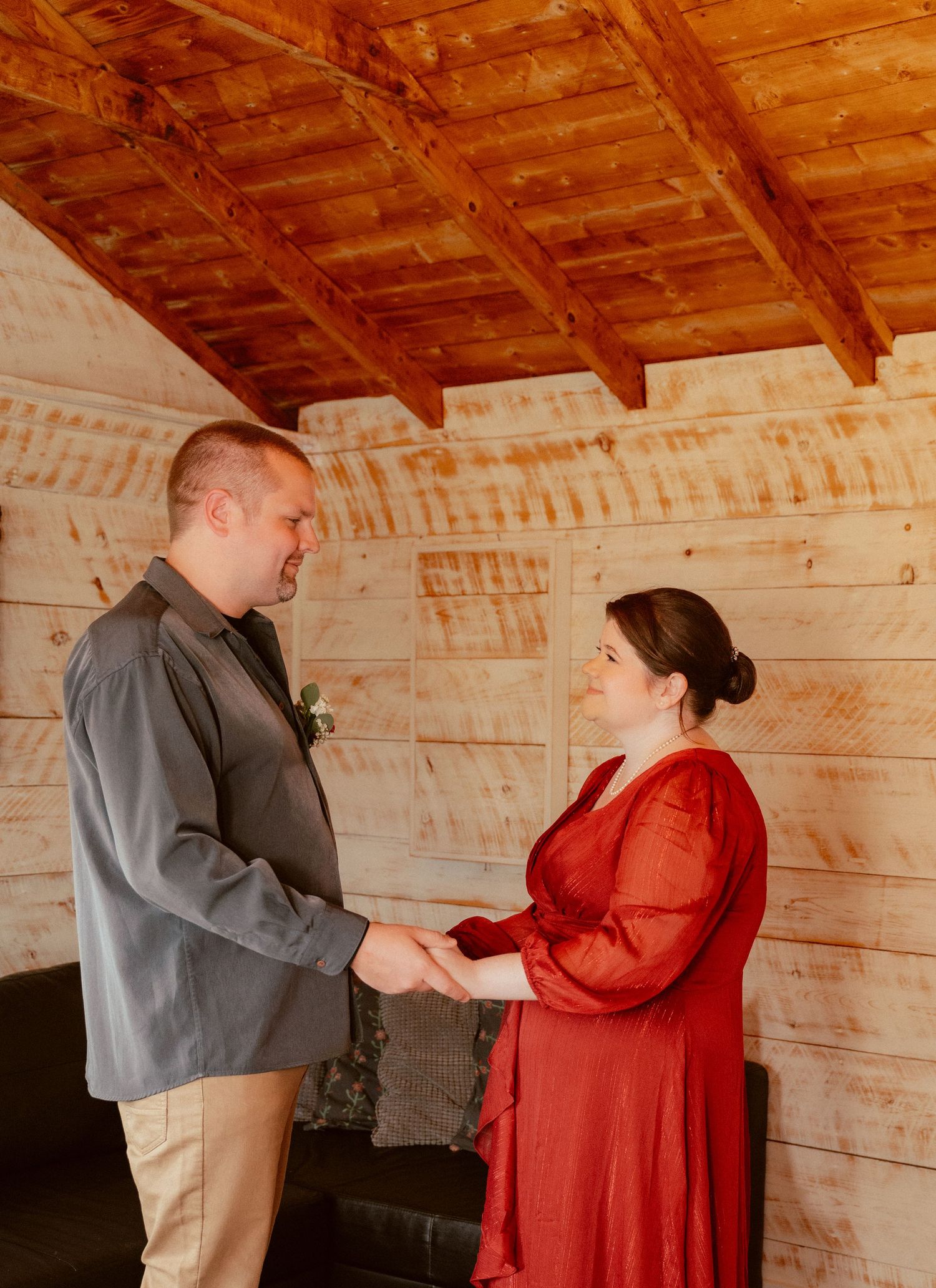 A couple holds hands intimately inside a rustic wooden cabin with exposed beams overhead.