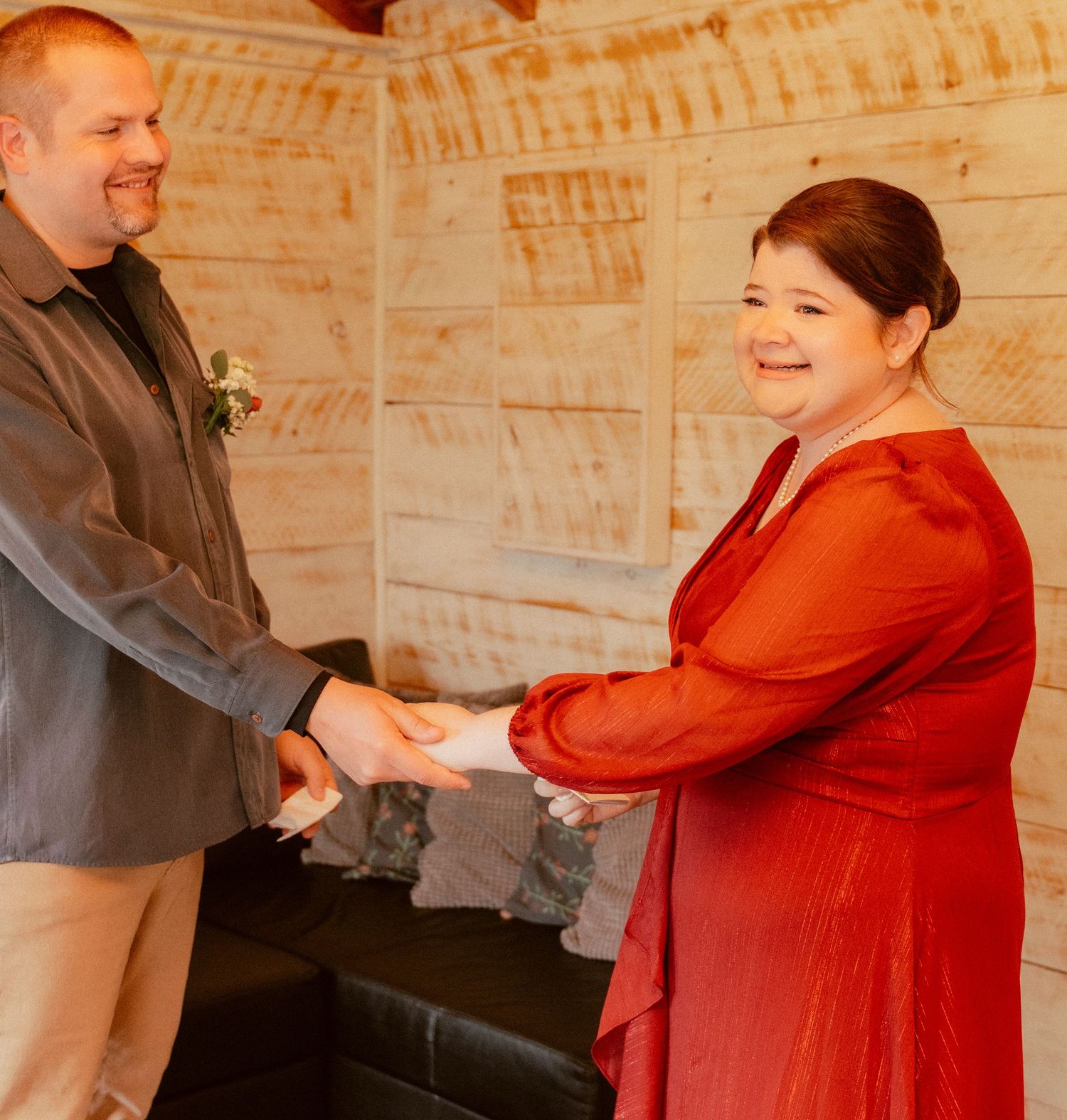 A wedding ceremony showing two people holding hands and smiling in a rustic indoor setting.