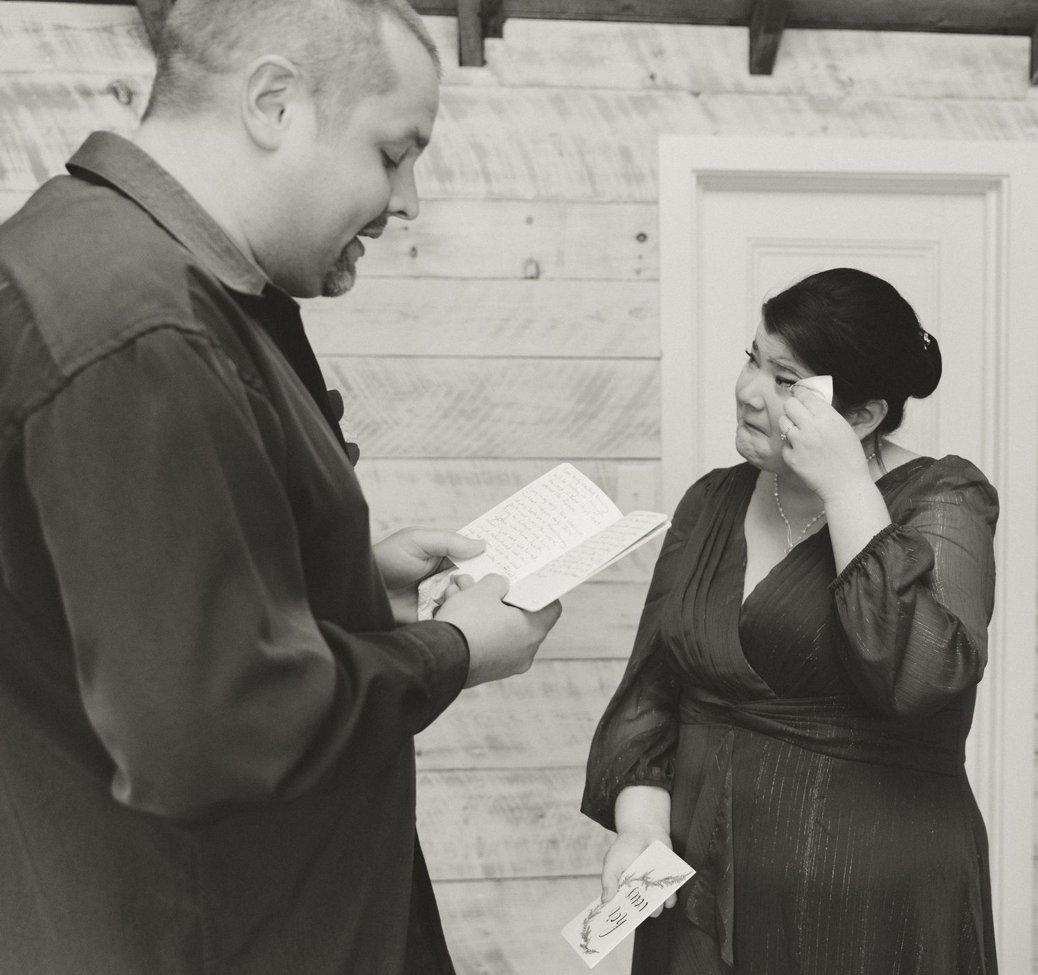A couple stands together reviewing papers in front of a rustic wooden wall.