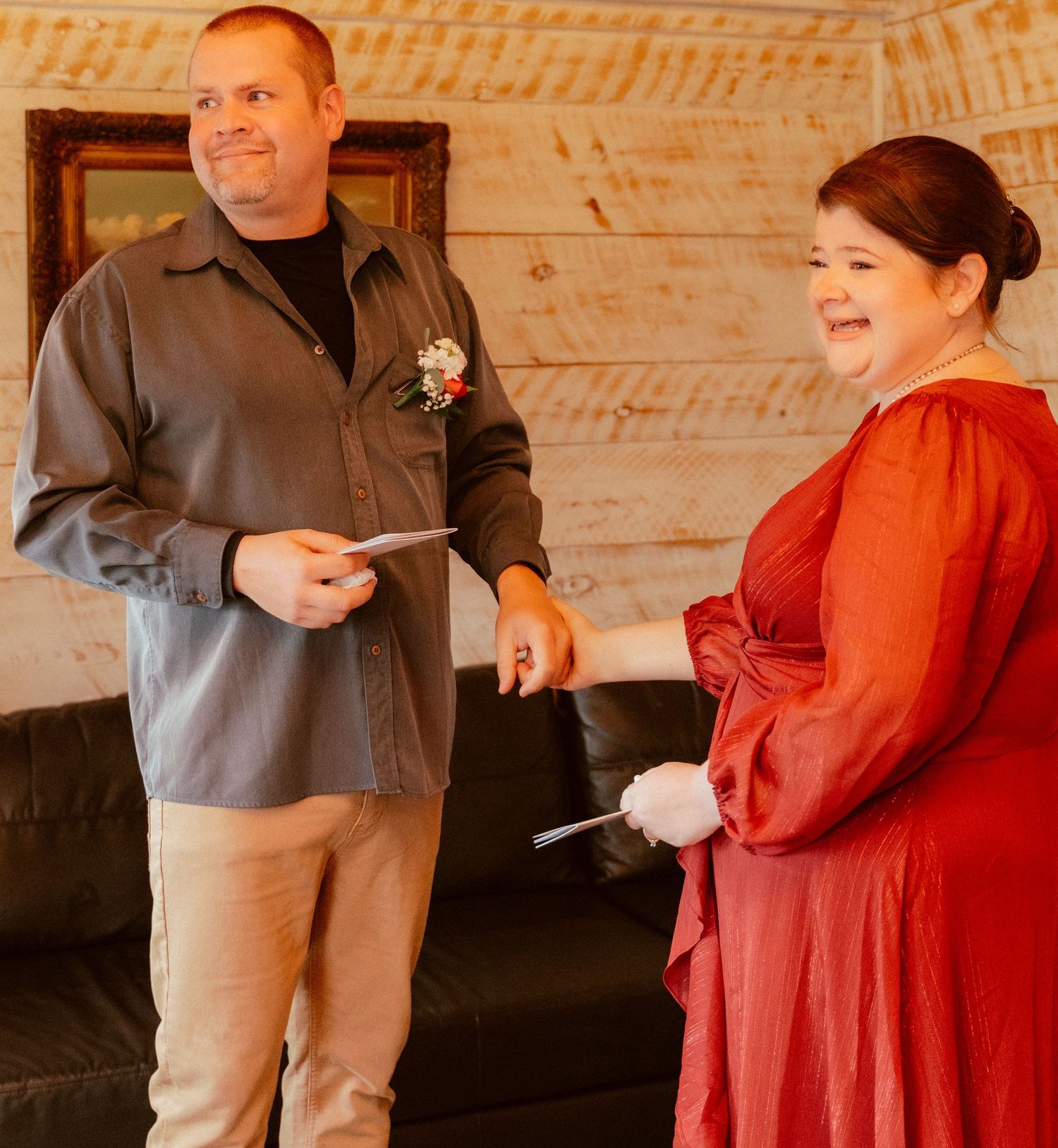 A couple shares a candid moment in formal attire, with a rustic wooden wall backdrop at an indoor venue.