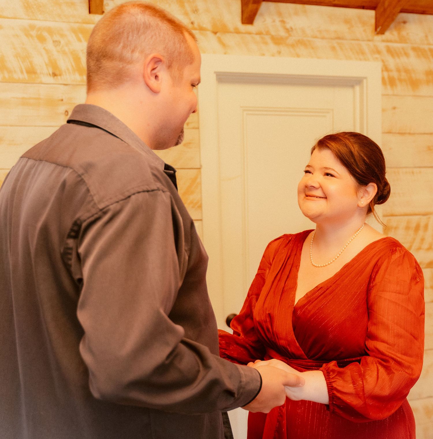 A couple shares a joyful moment while holding hands in a rustic indoor setting.