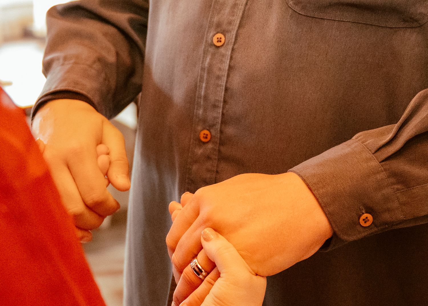 Close-up shot of hands holding each other with brown shirt and red dress visible.