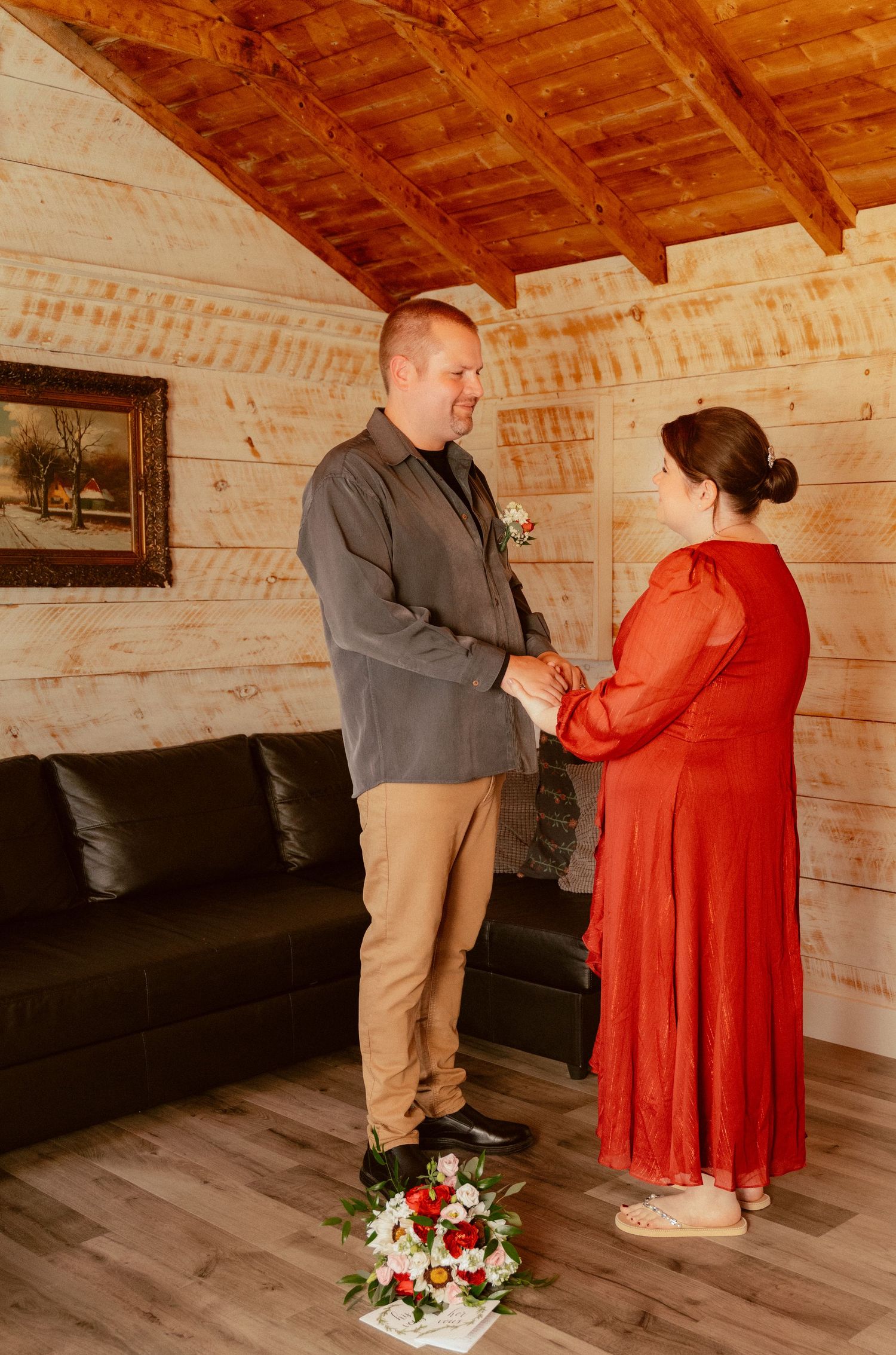 A couple exchanges vows in a cozy cabin interior with exposed wooden beams and walls.
