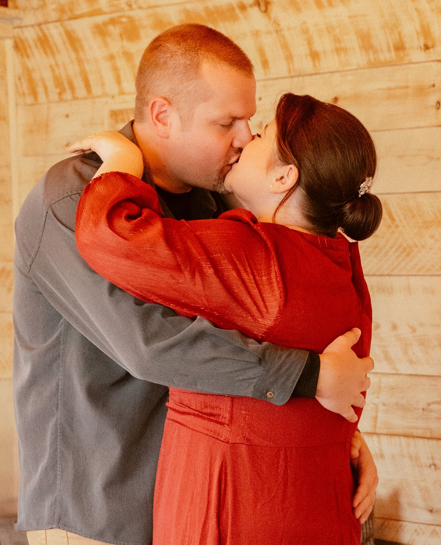 A romantic embrace captured indoors with soft lighting and wooden wall backdrop.
