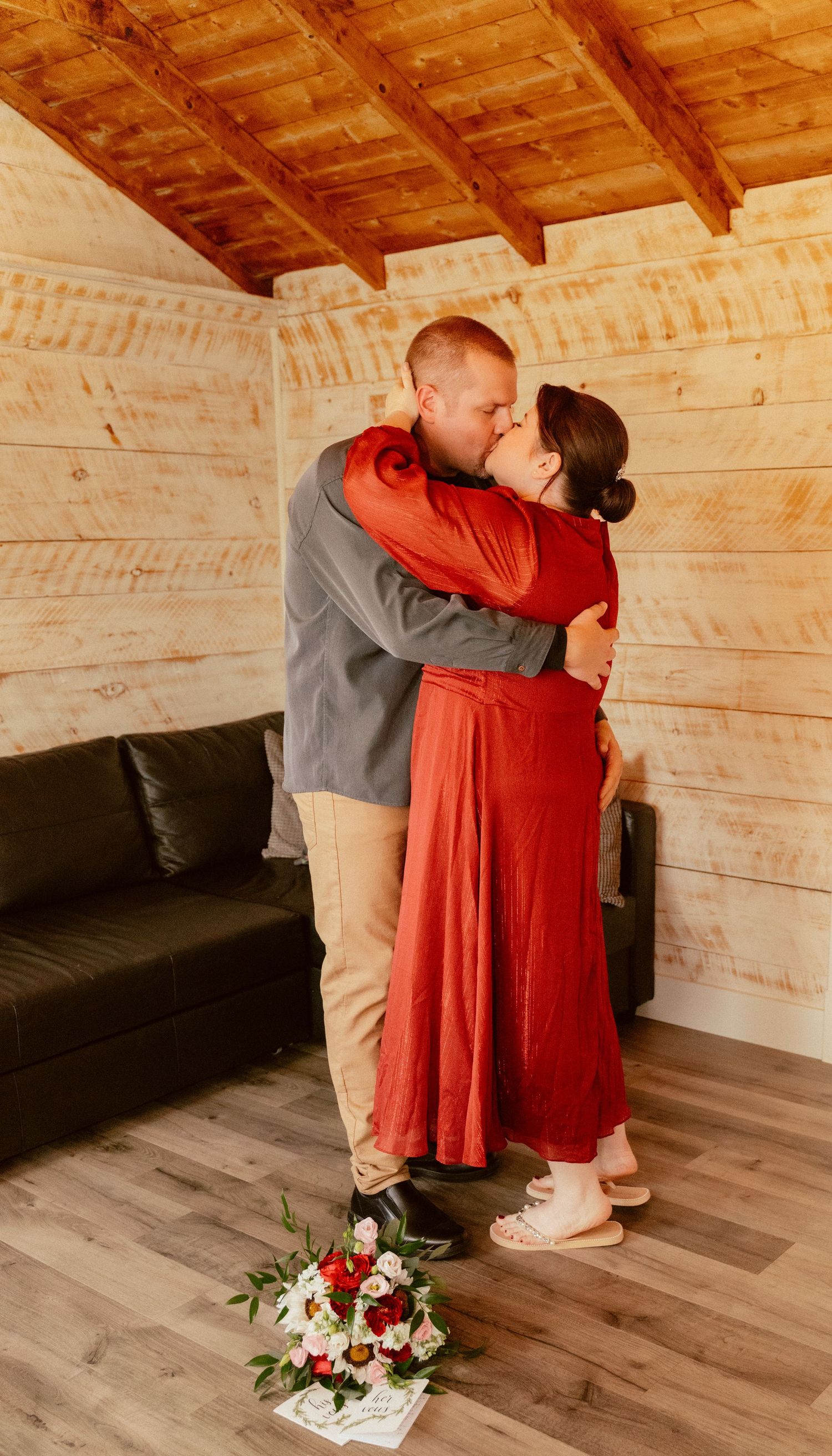 A romantic embrace between newlyweds in a cozy cabin with exposed wood beams and floral decor.