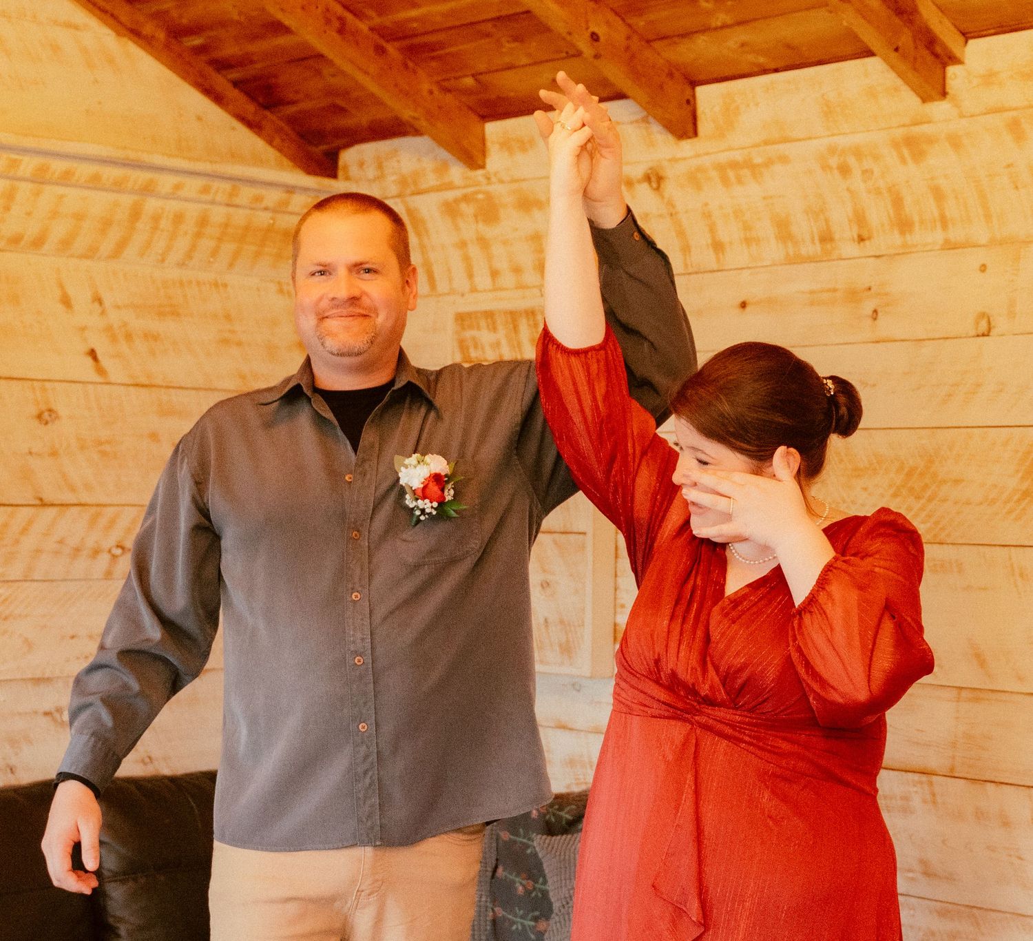 A joyful celebration moment between two people in formal attire inside a wooden cabin.