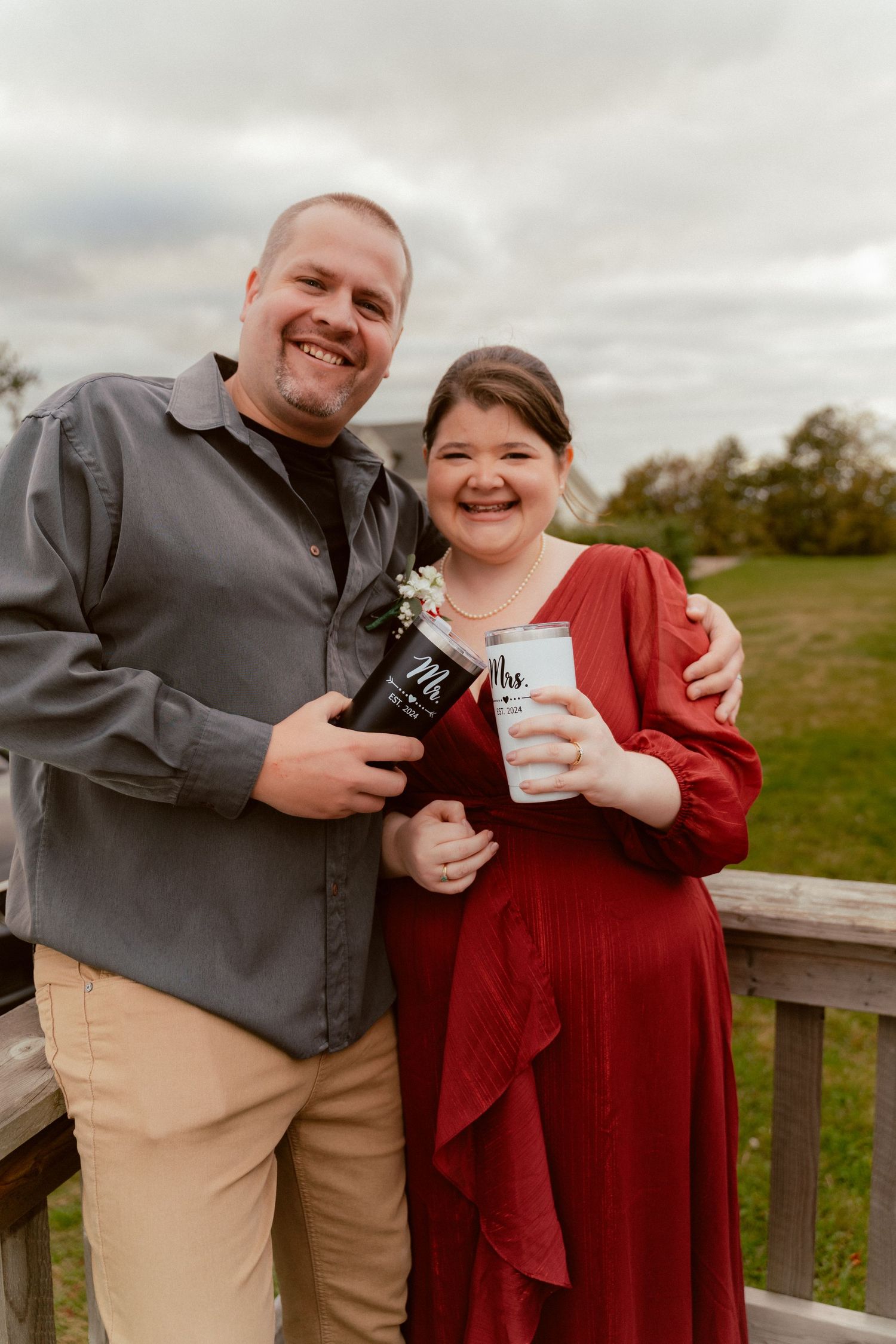 Happy couple holding drinks and embracing on outdoor deck under cloudy sky.