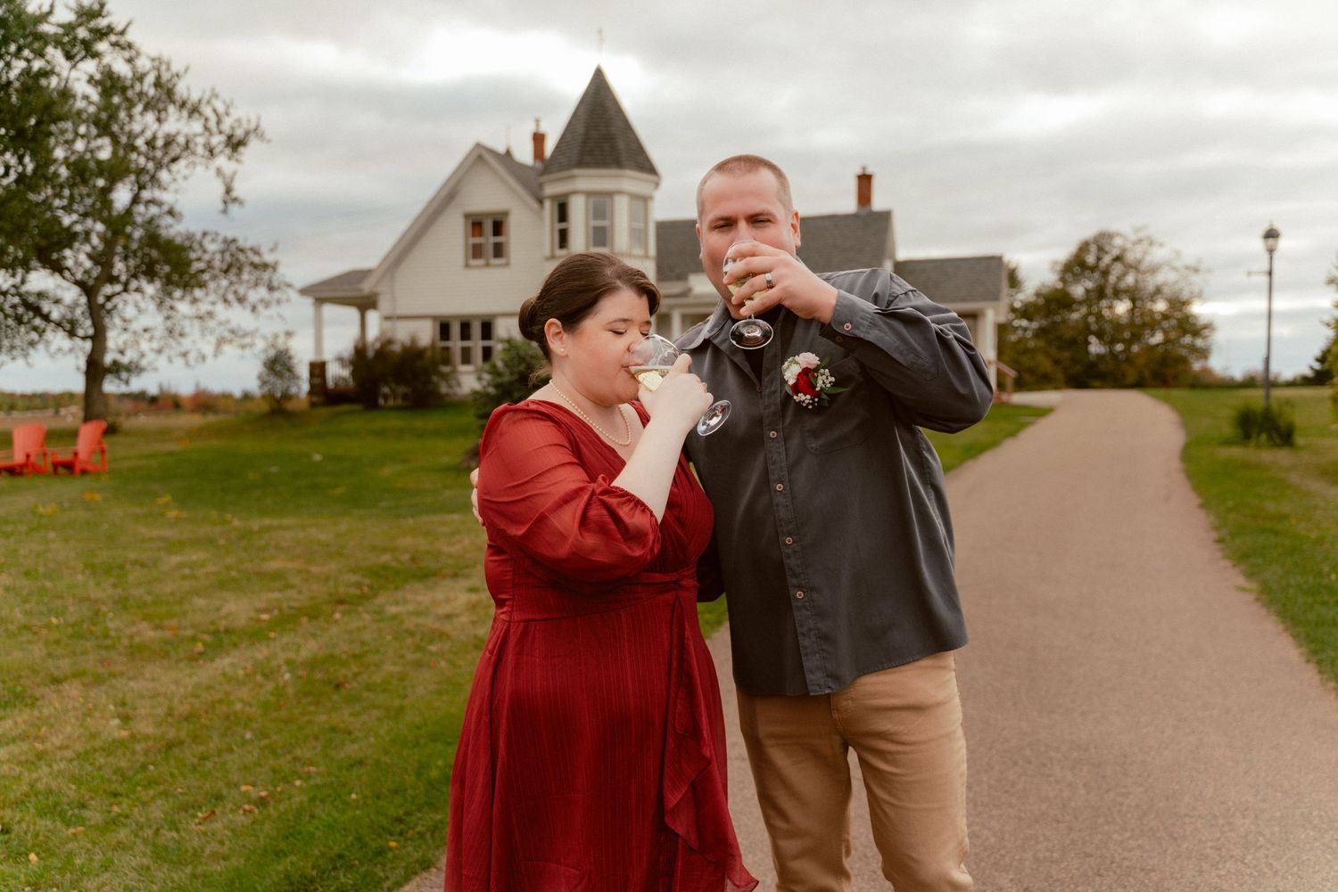 A couple shares a joyful moment outside a Victorian-style house on a cloudy day.