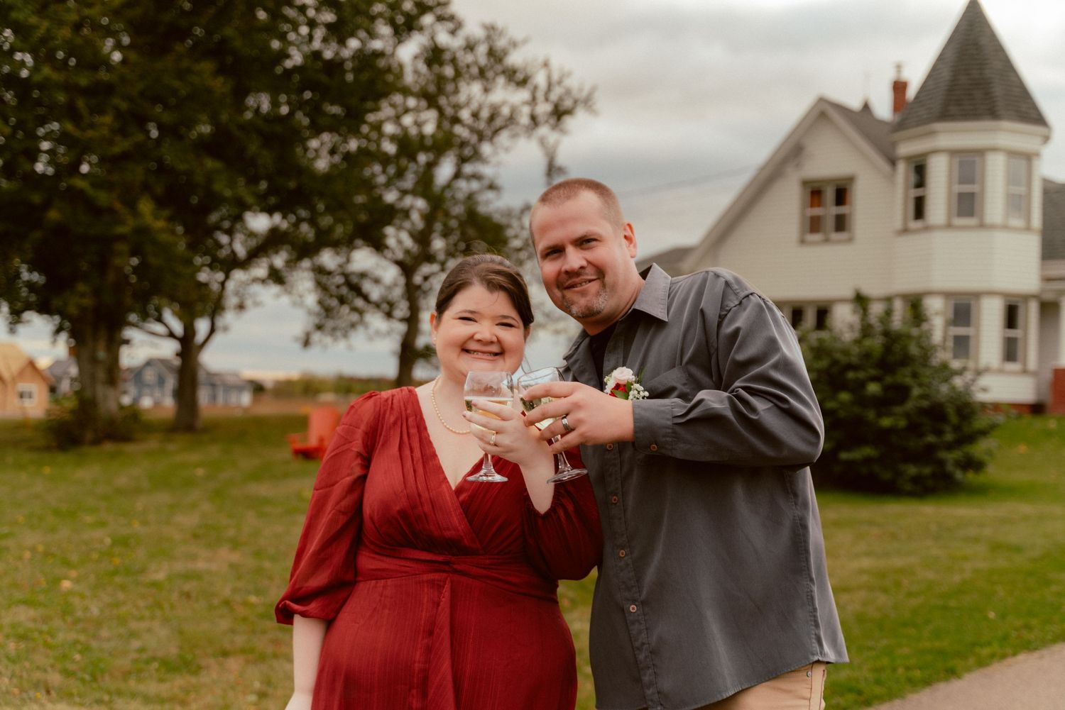 A happy couple shares a laugh while holding papers in front of a Victorian-style house.