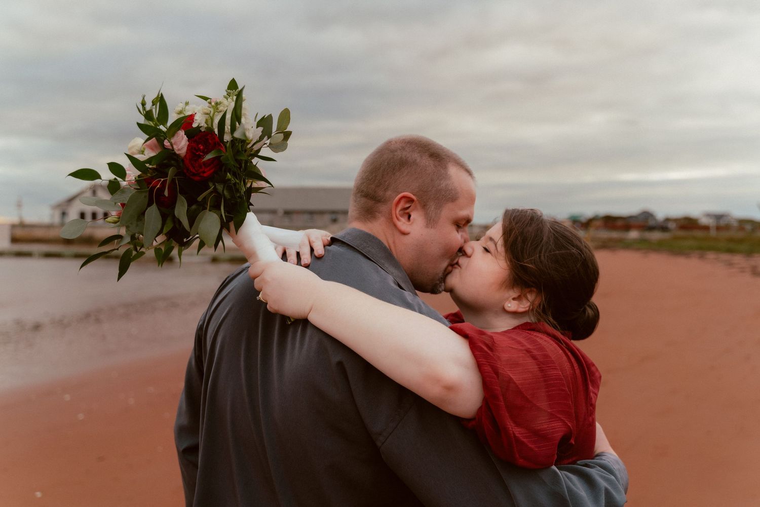 A romantic sunset embrace with moody clouds and floral bouquet.