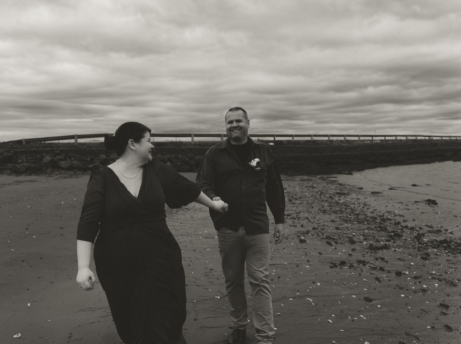 Two people share a joyful moment while dancing on a beach under an overcast sky.