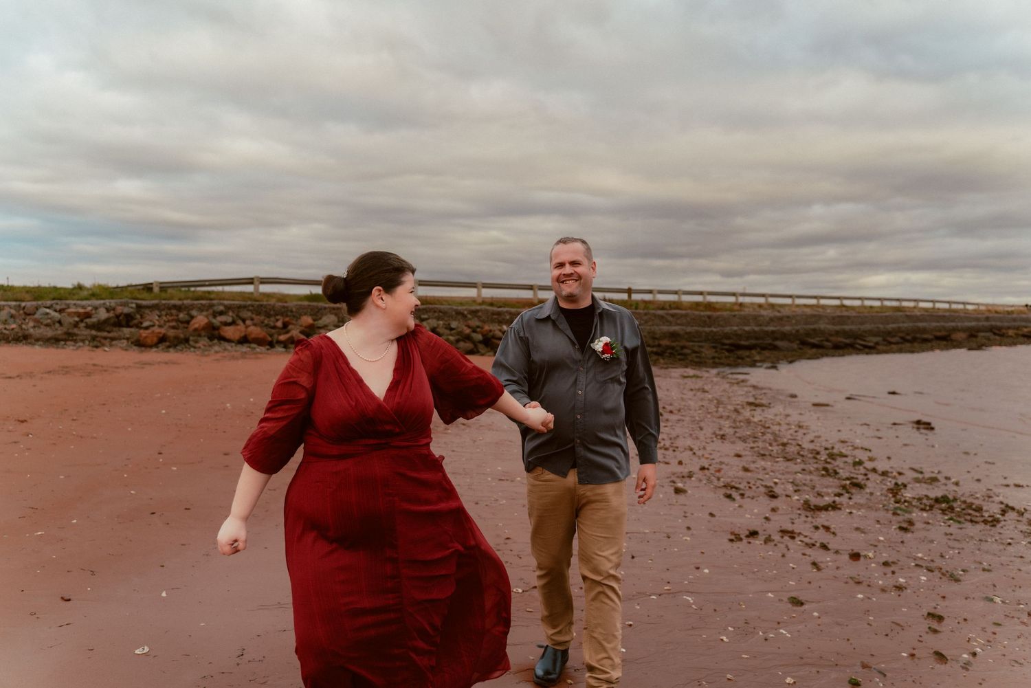 Two people walking and laughing together on a sandy beach under cloudy skies.