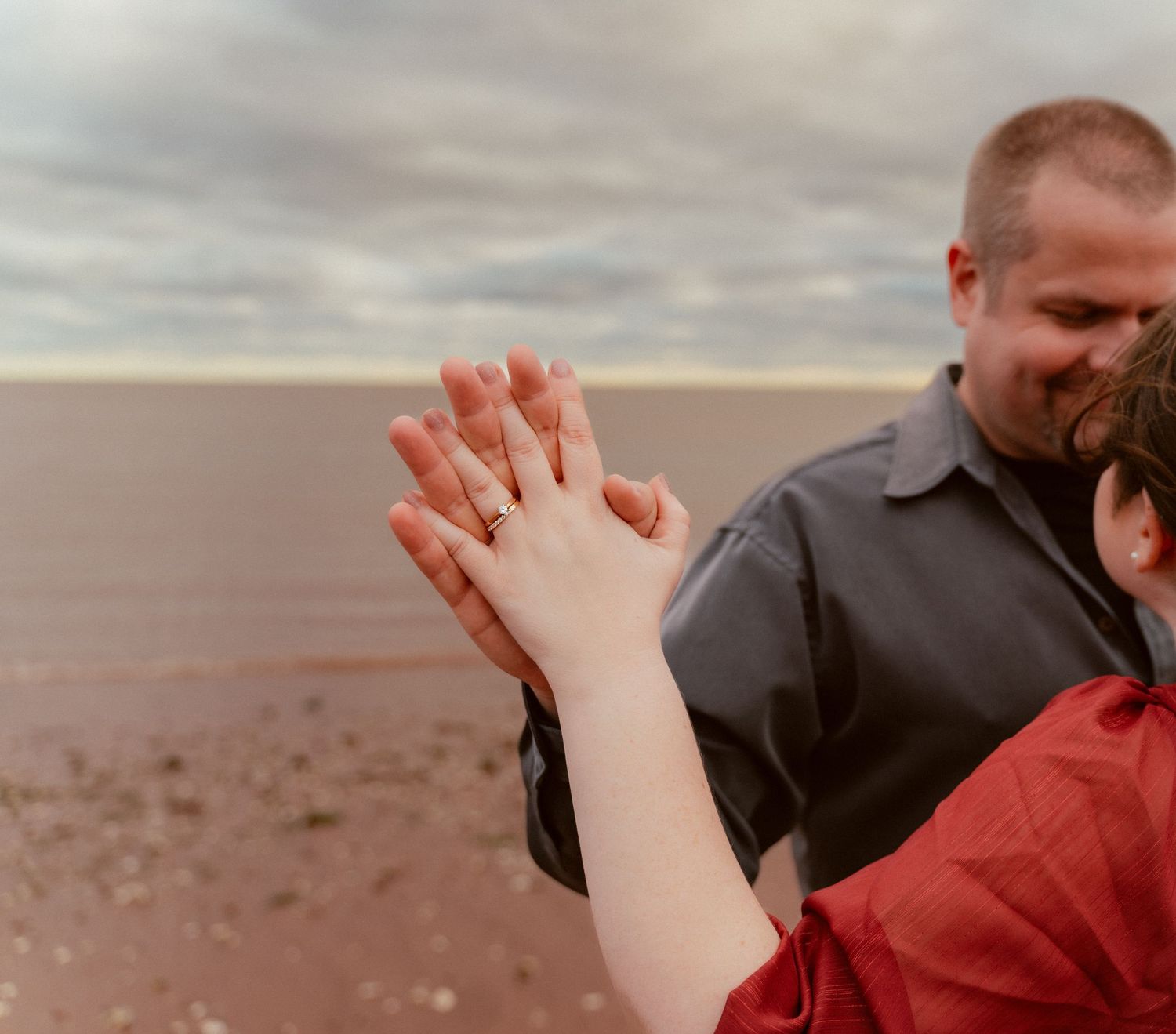 A couple shows off their wedding rings against a coastal backdrop.
