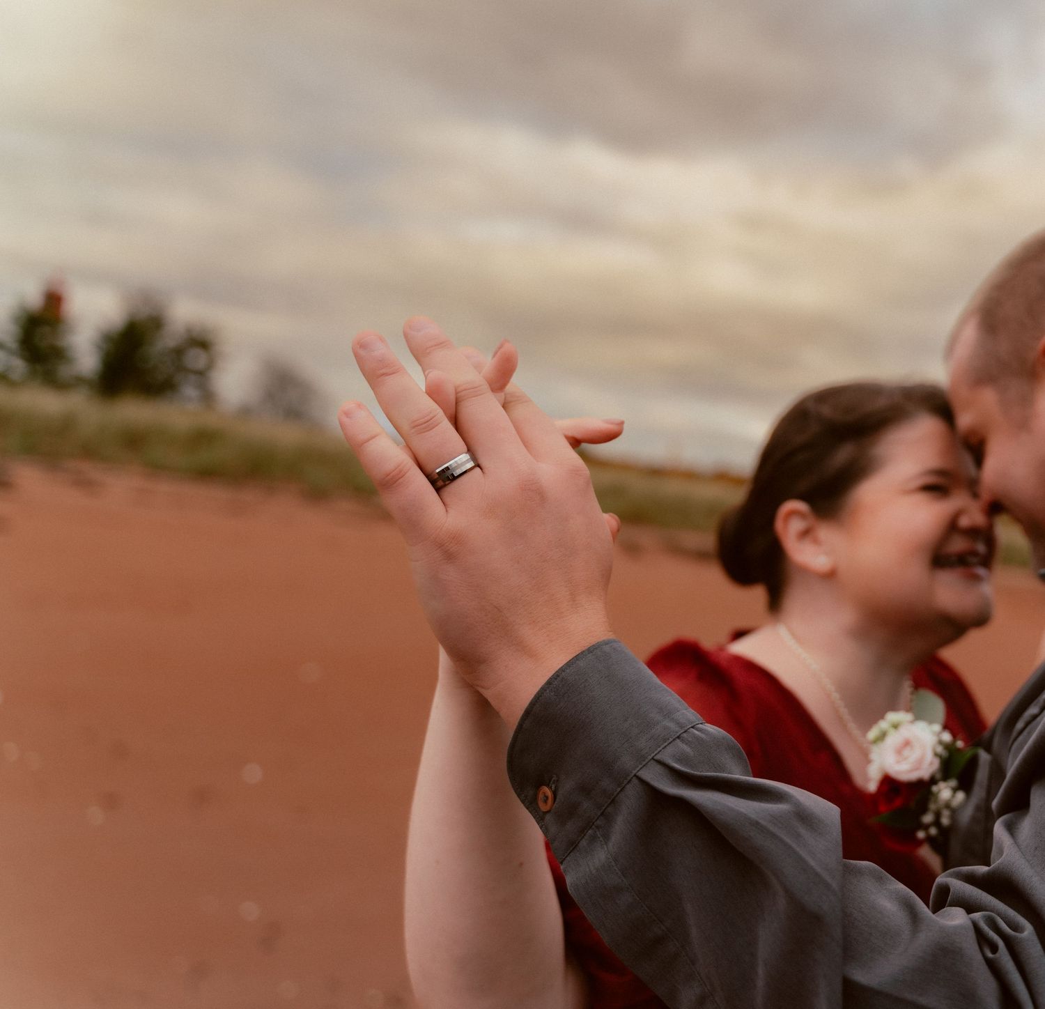 A close-up of hands with a ring against a dramatic cloudy sky and red earth landscape.