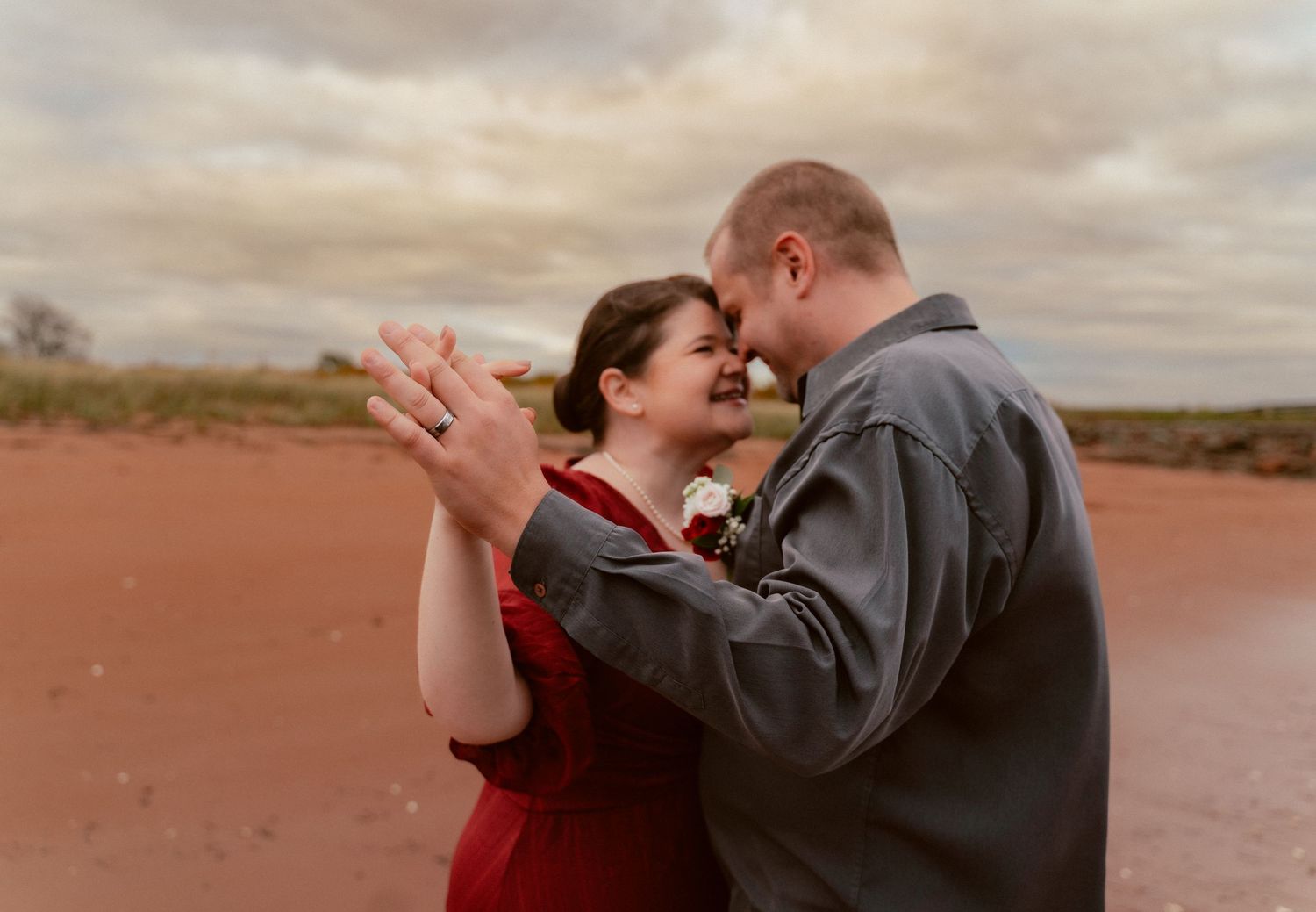 A romantic moment captured against a moody desert backdrop with red soil and cloudy skies.