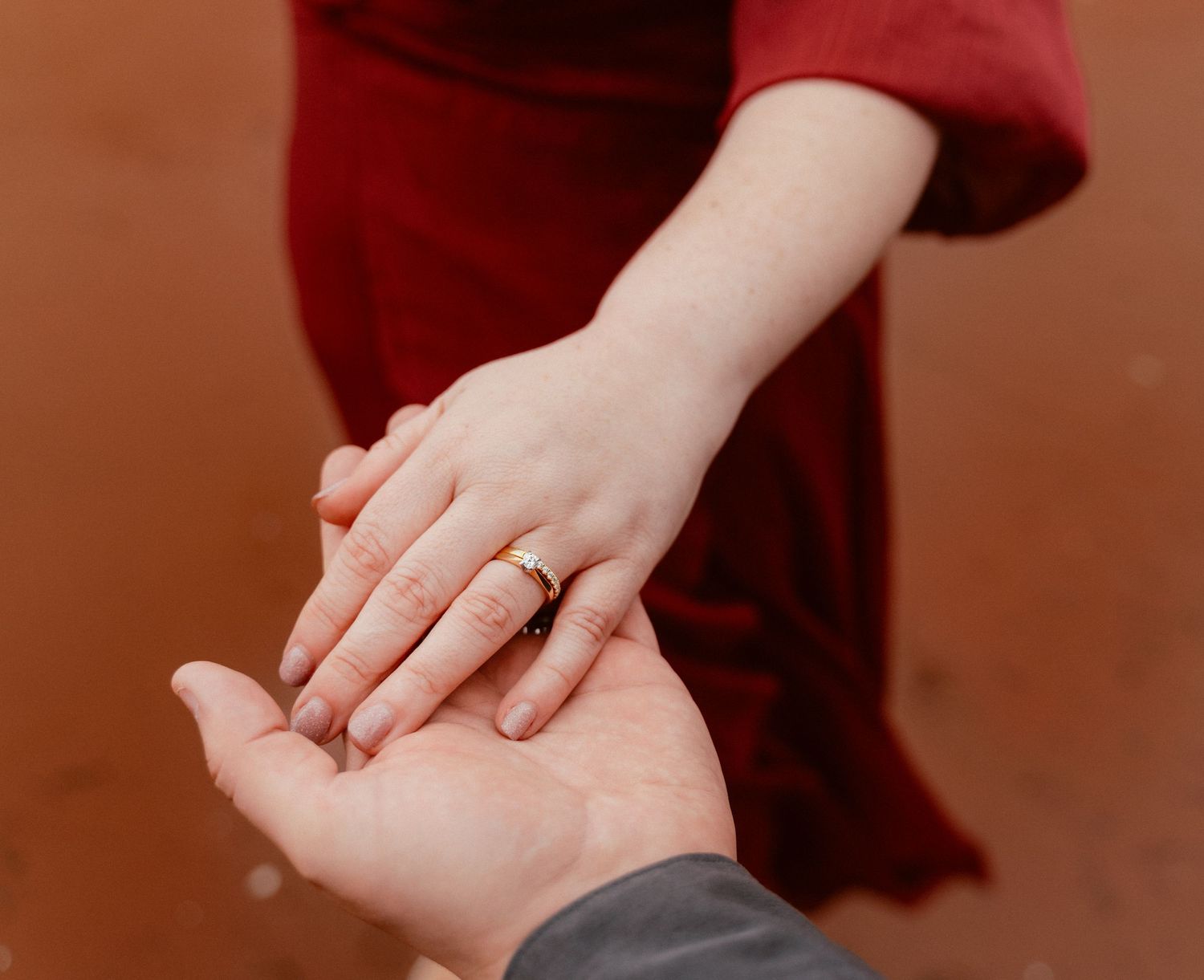 Close-up of hands holding with engagement ring visible against a red dress backdrop.
