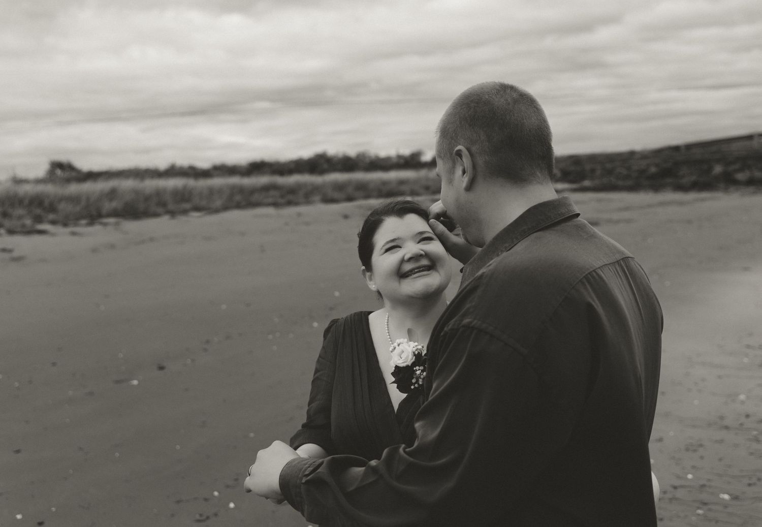 A tender moment between two people sharing laughter on an overcast beach.